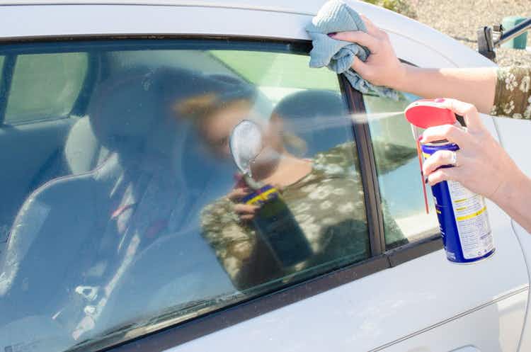 A person spraying WD-40 on a car window.