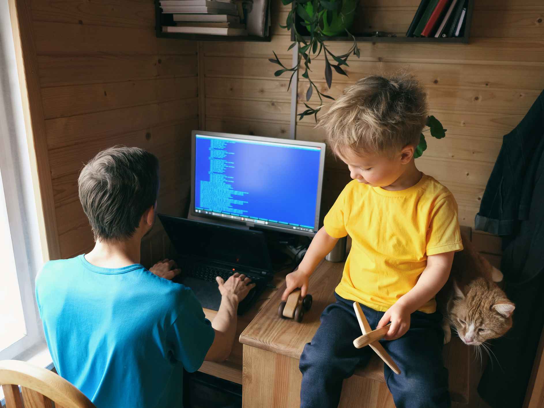 dad works on computer with small boy watching
