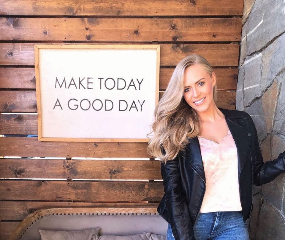 woman smiles next to a sign that reads Make Today a Good Day
