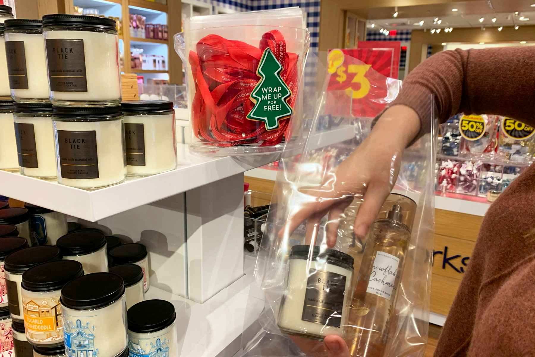 A woman in Bath & Body Works, packaging her candles and fragrance into a plastic gift bag.