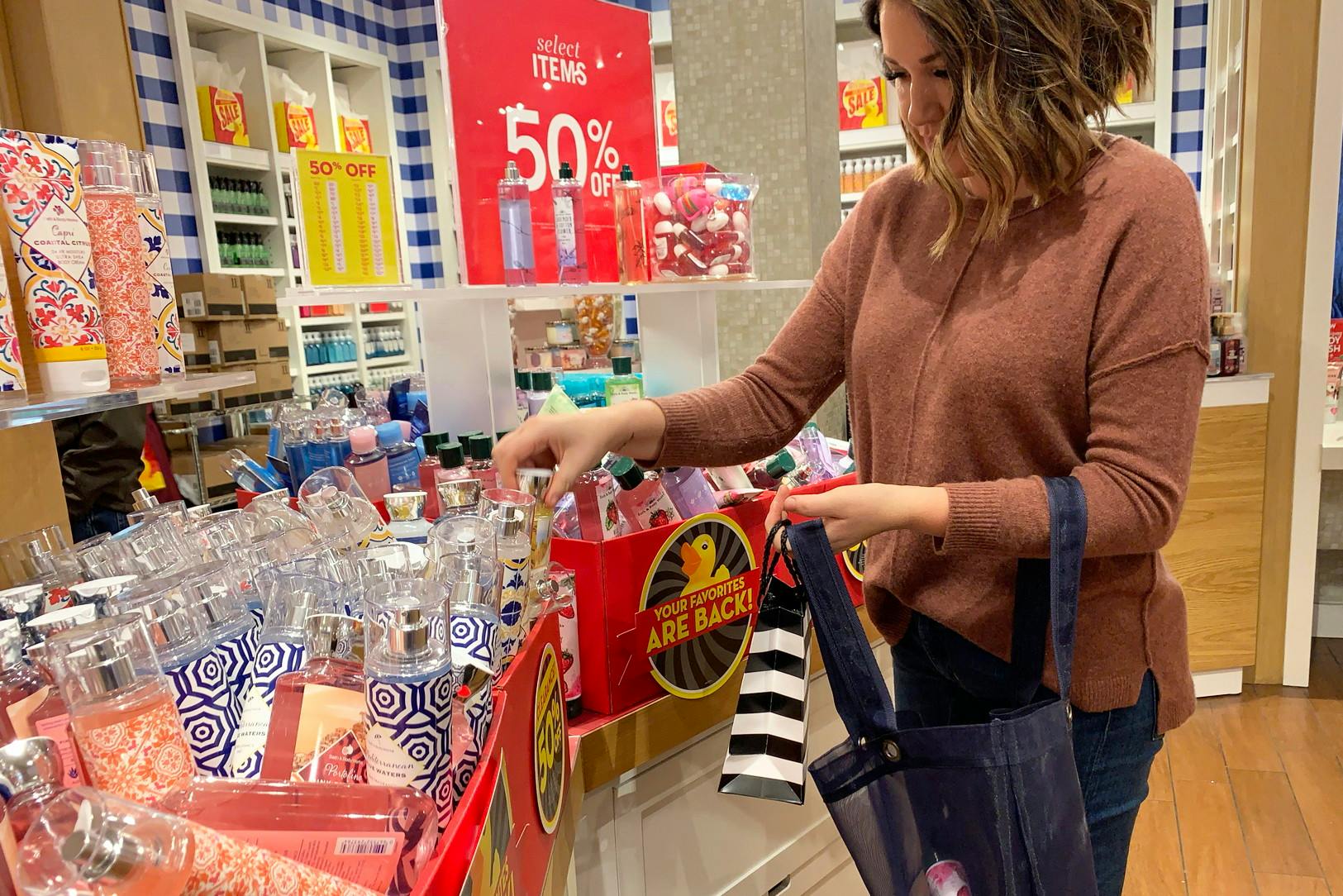A woman holding a bag and choosing products out of a sale box inside Bath & Body Works.