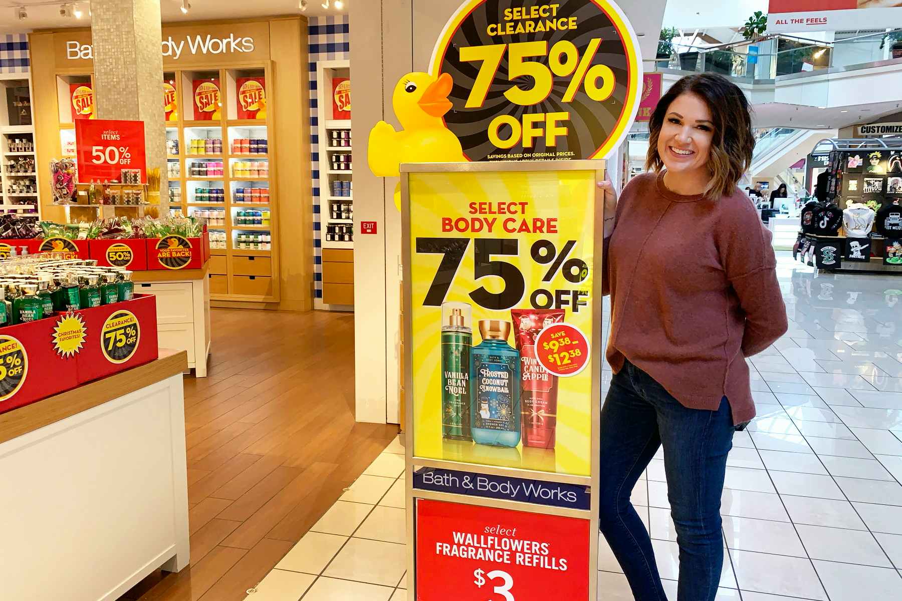 A woman standing next to a sign outside of Bath & Body Works advertising their 75% off Semi-Annual clearance sale.