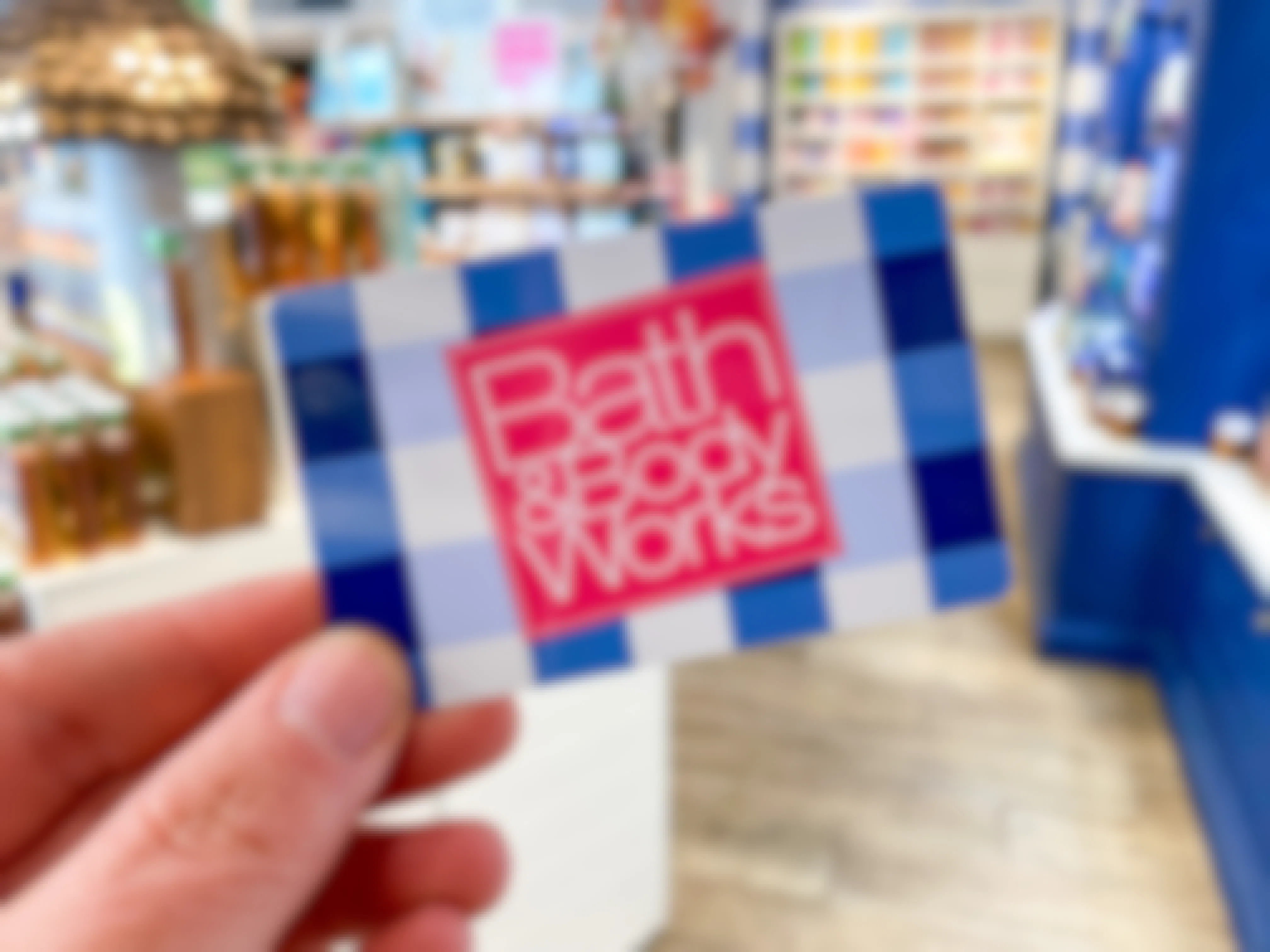 A person's hand holding up a Bath & Body Works gift card inside of a Bath & Body Works.