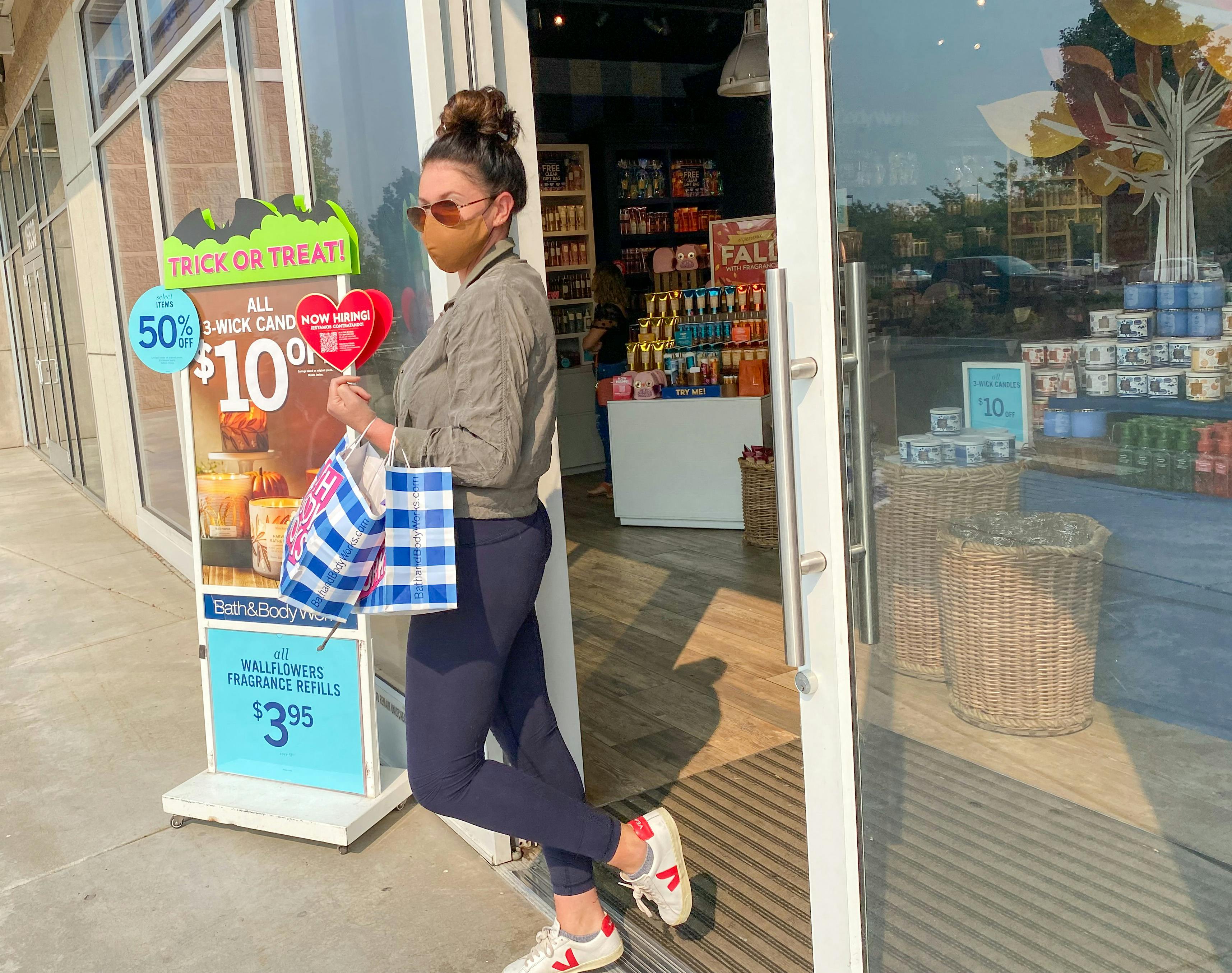 A woman walking out of a bath and body works store carrying shopping bags.