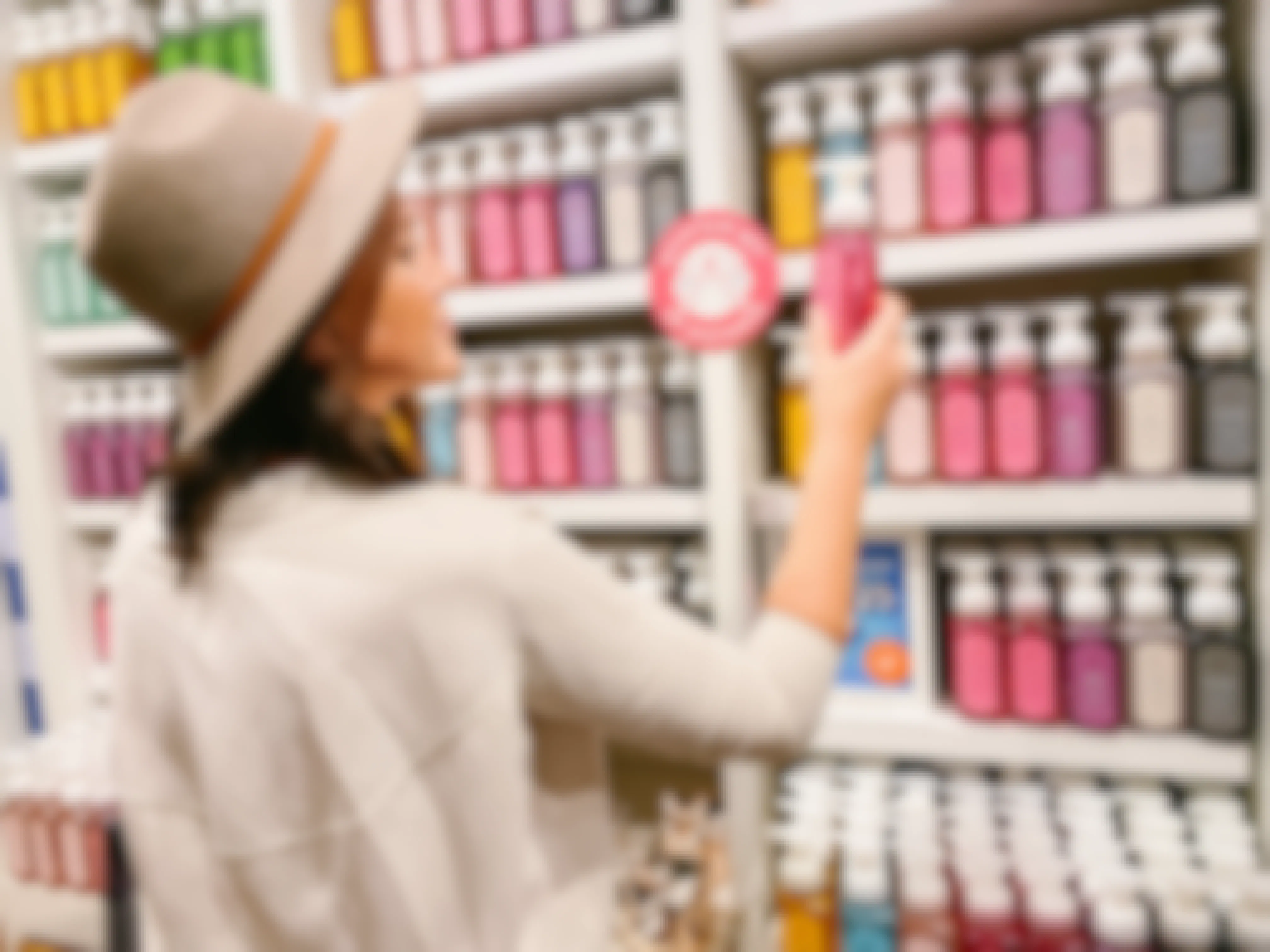 A woman standing in front of the wall display of hand soaps at Bath & Body Works, holding up a bottle of soap and looking at it.