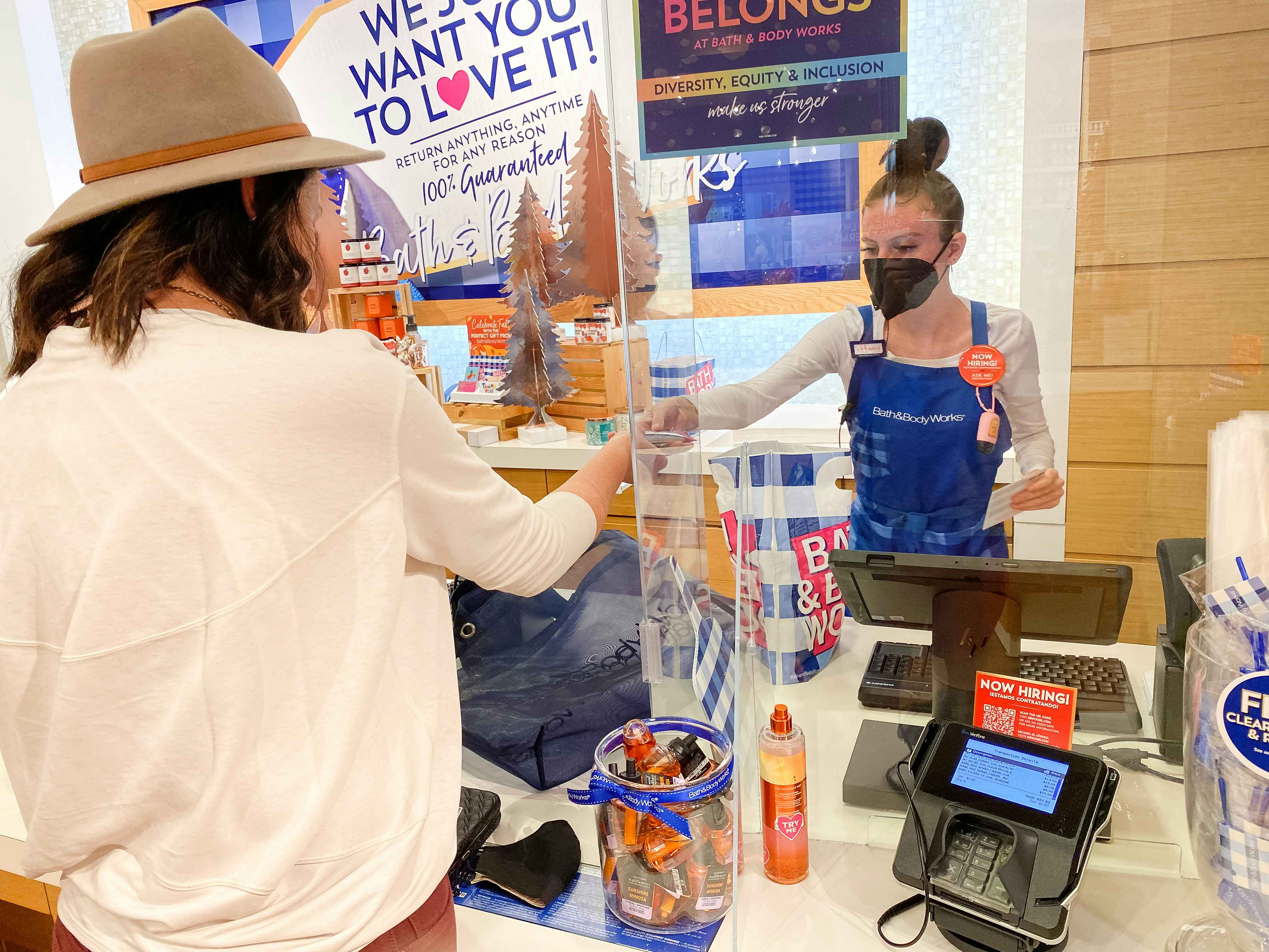 A woman standing at the checkout counter at Bath & Body Works, handing something to the cashier.