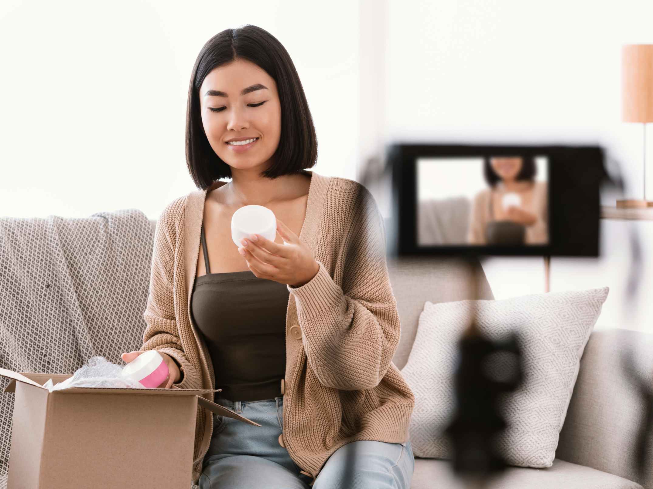 A woman taking products out of a box while sitting on a couch in front of a camera.