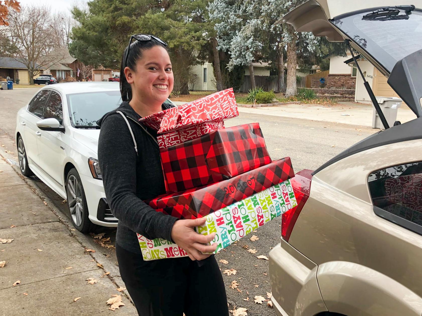A person holding a stack of presents by an open vehicle trunk