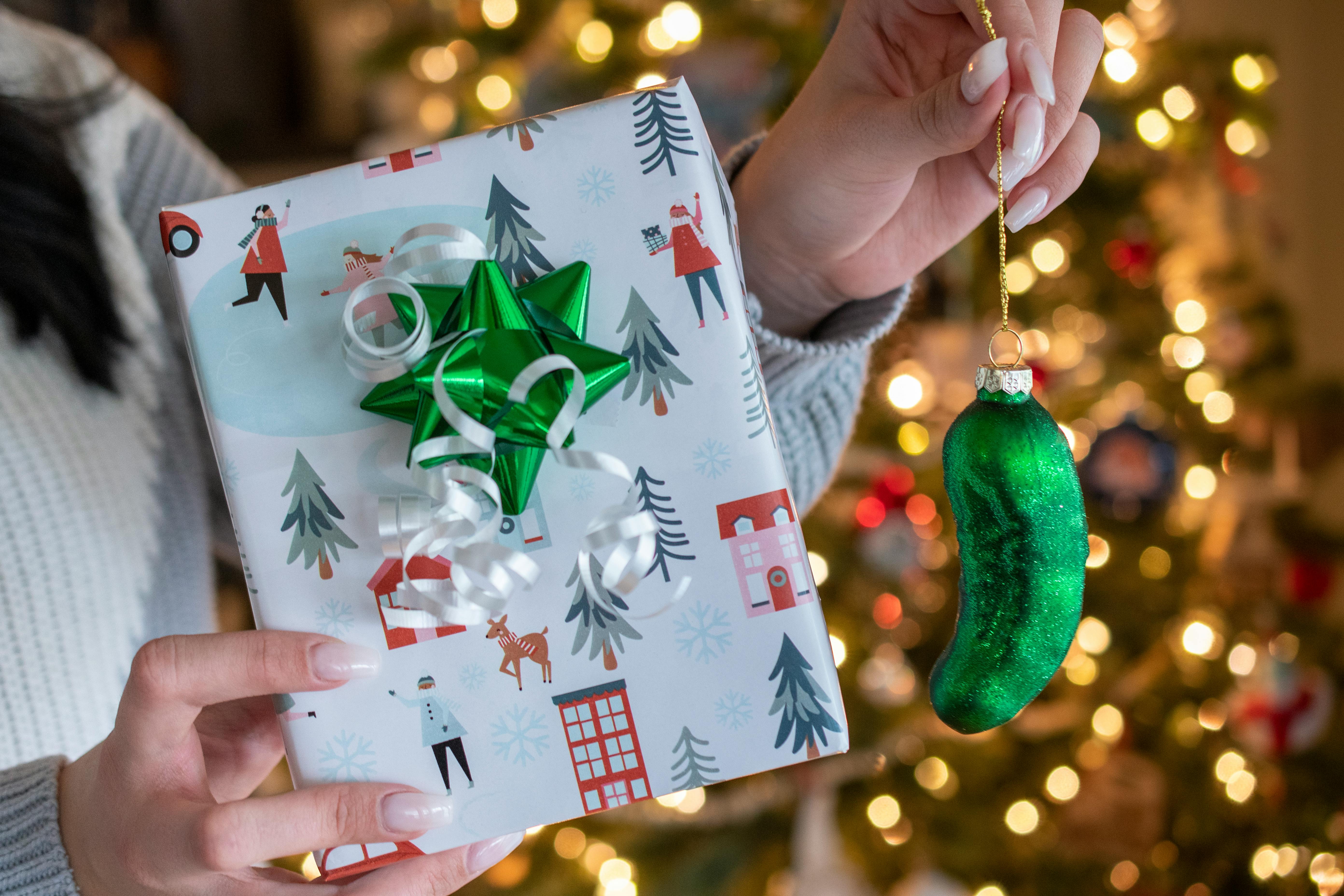 An green pickle Christmas ornament held next to a gift box.