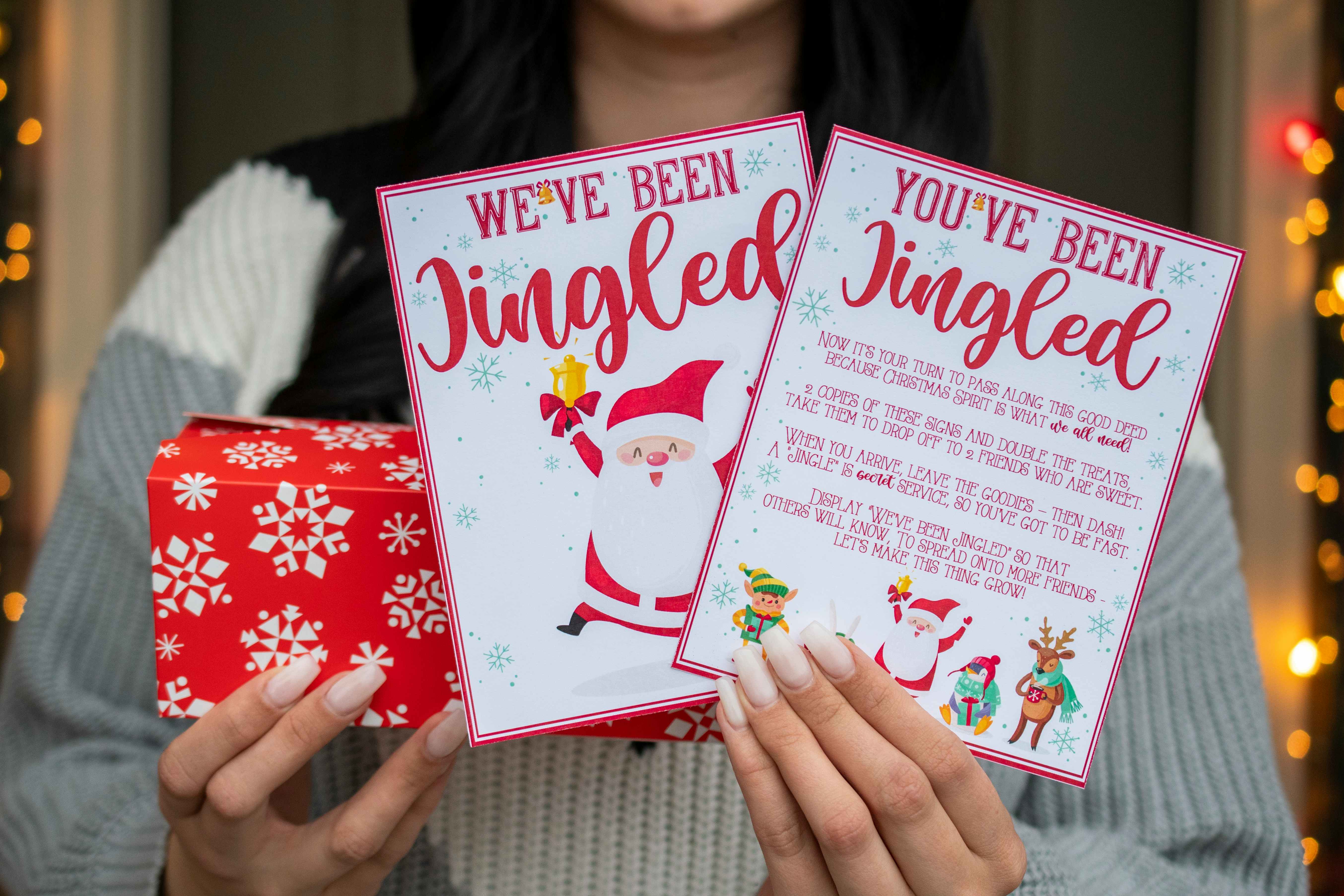 Someone holding a wrapped present and two cards, one saying "we've been jingled" and the other saying, "you've been jingled" with an explanation of the game