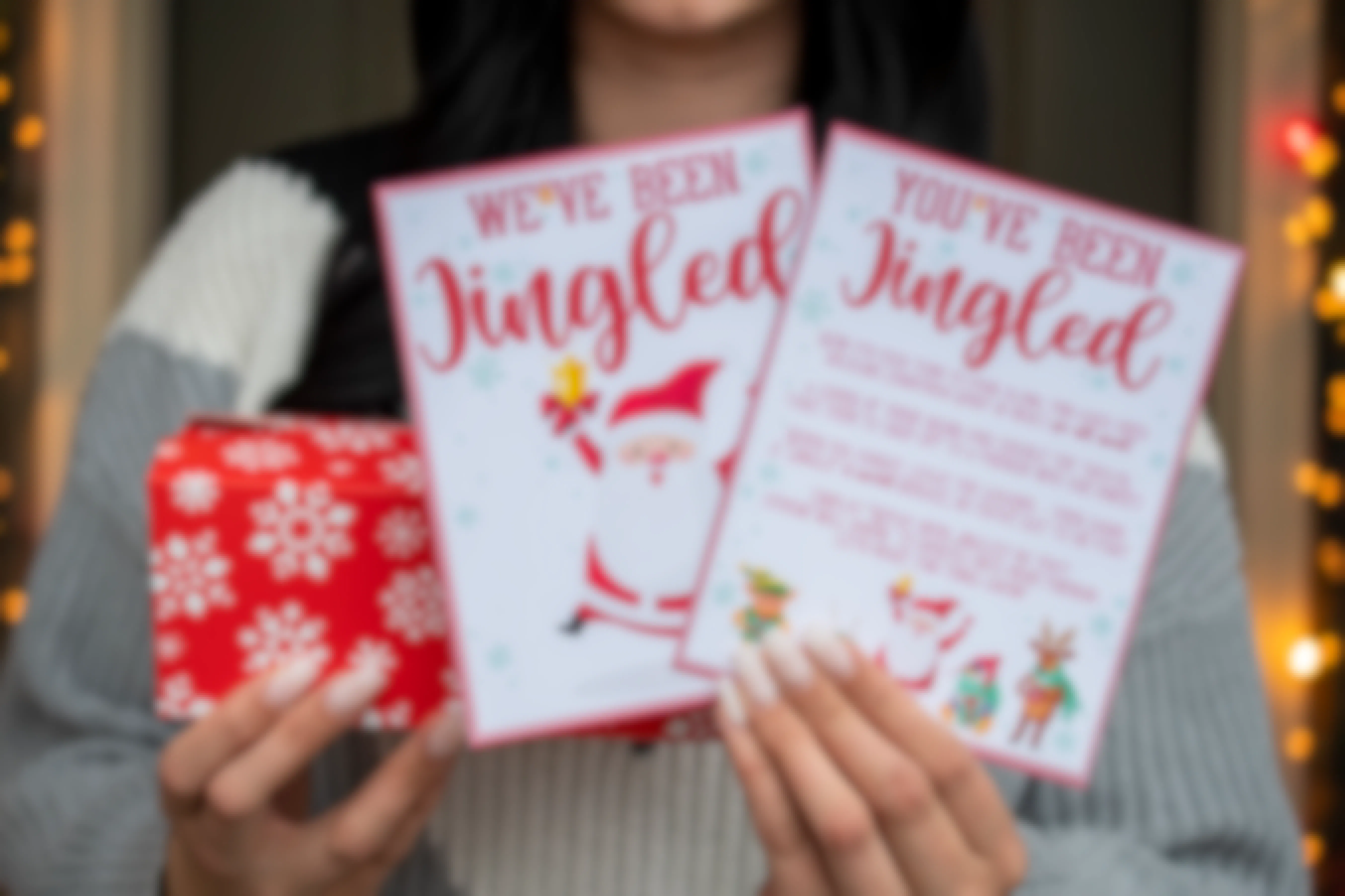 Someone holding a wrapped present and two cards, one saying "we've been jingled" and the other saying, "you've been jingled" with an explanation of the game