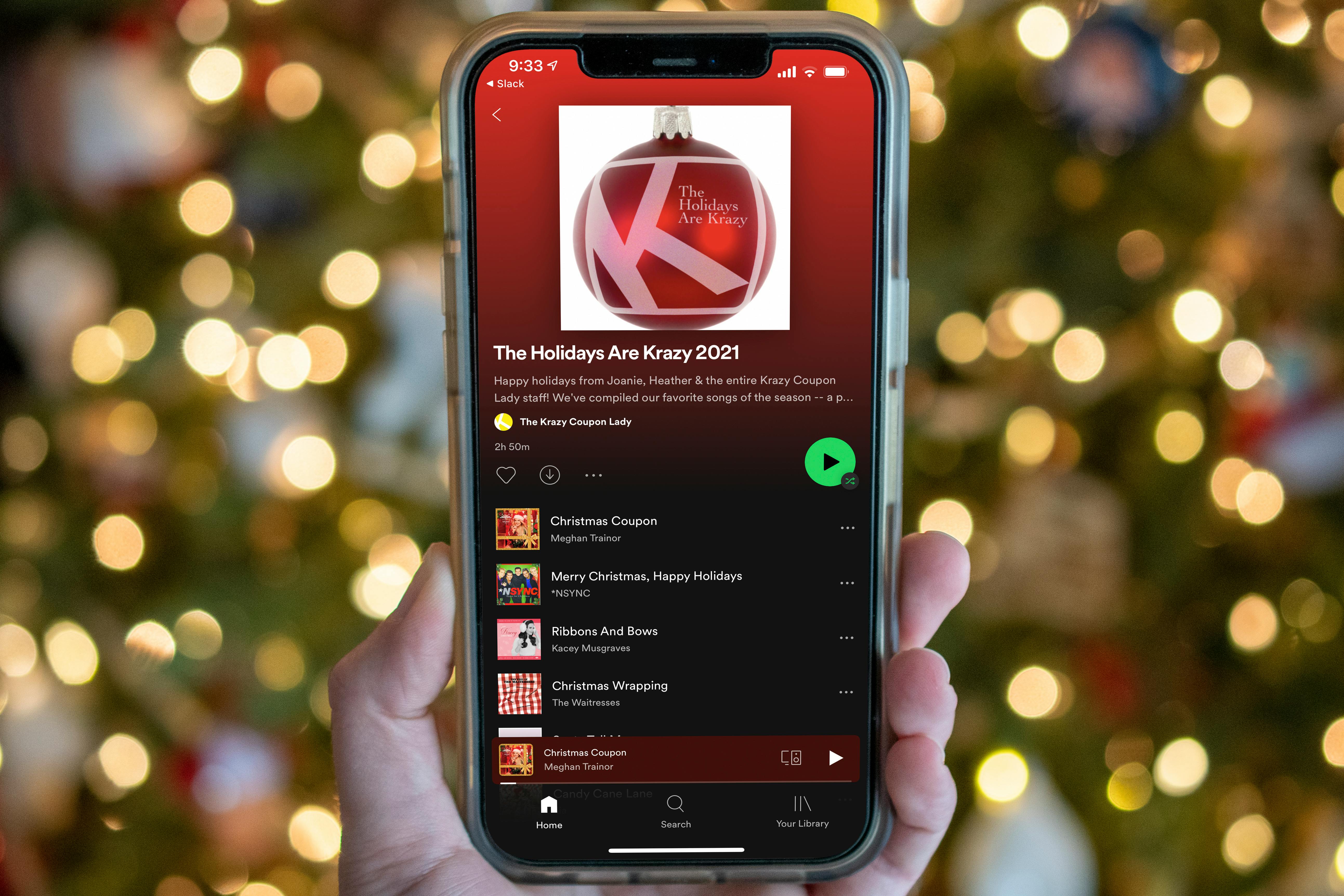 A person holding up a cell phone with a Christmas tree in the background displaying a Spotify Christmas playlist