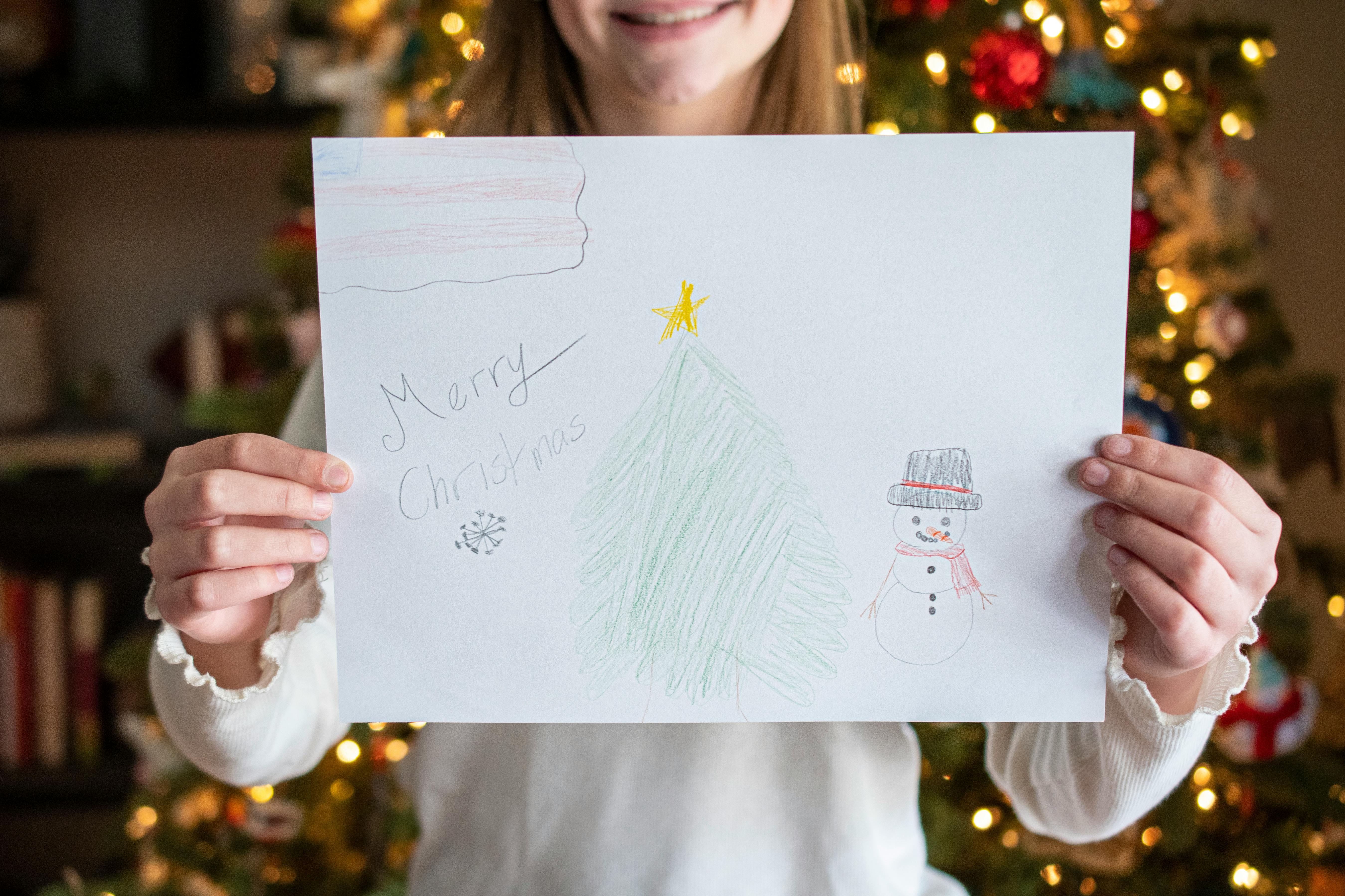 A little girl holding a drawing in front of a Christmas tree.