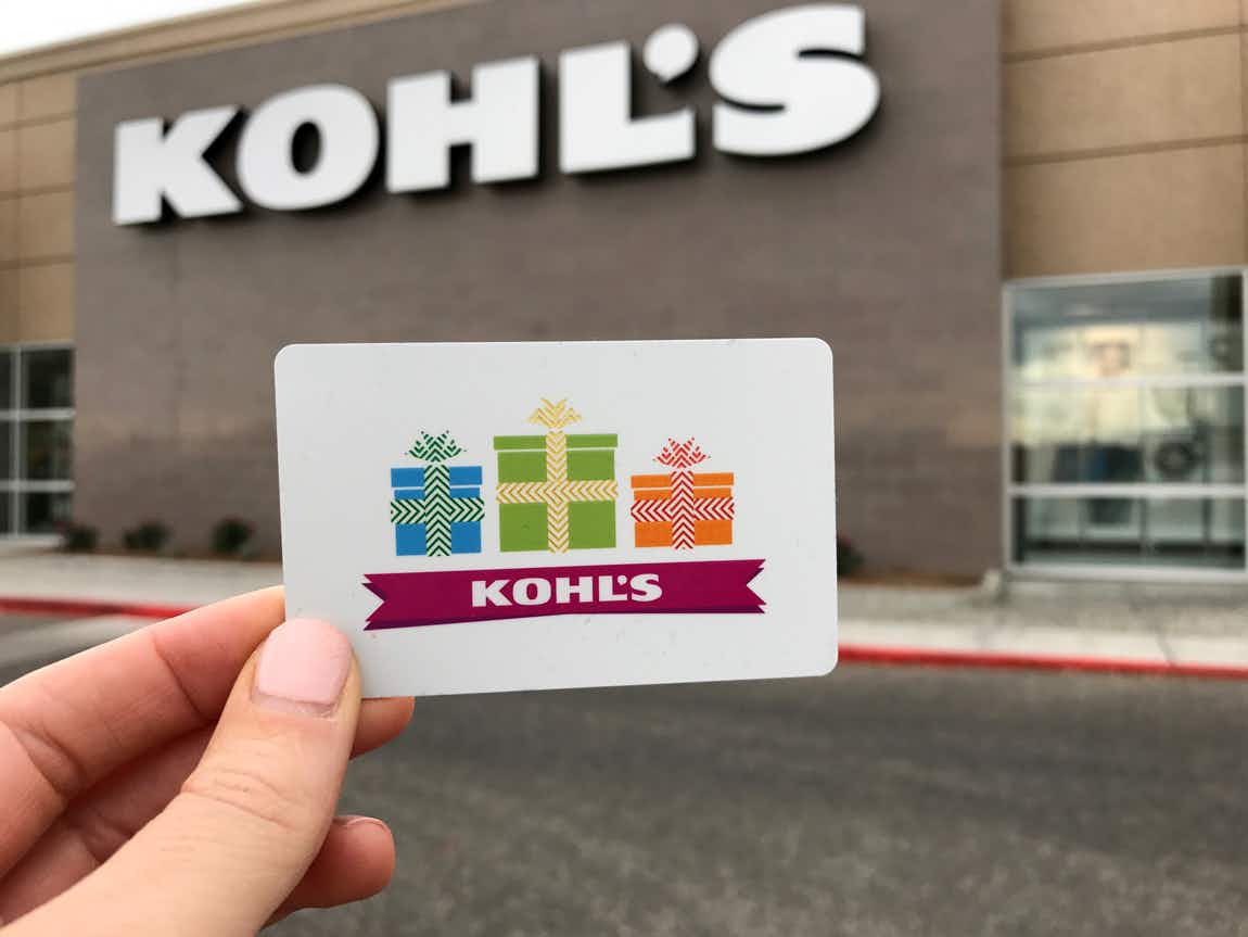 Hand holding a Kohl's Gift Card in front of a Kohl's 