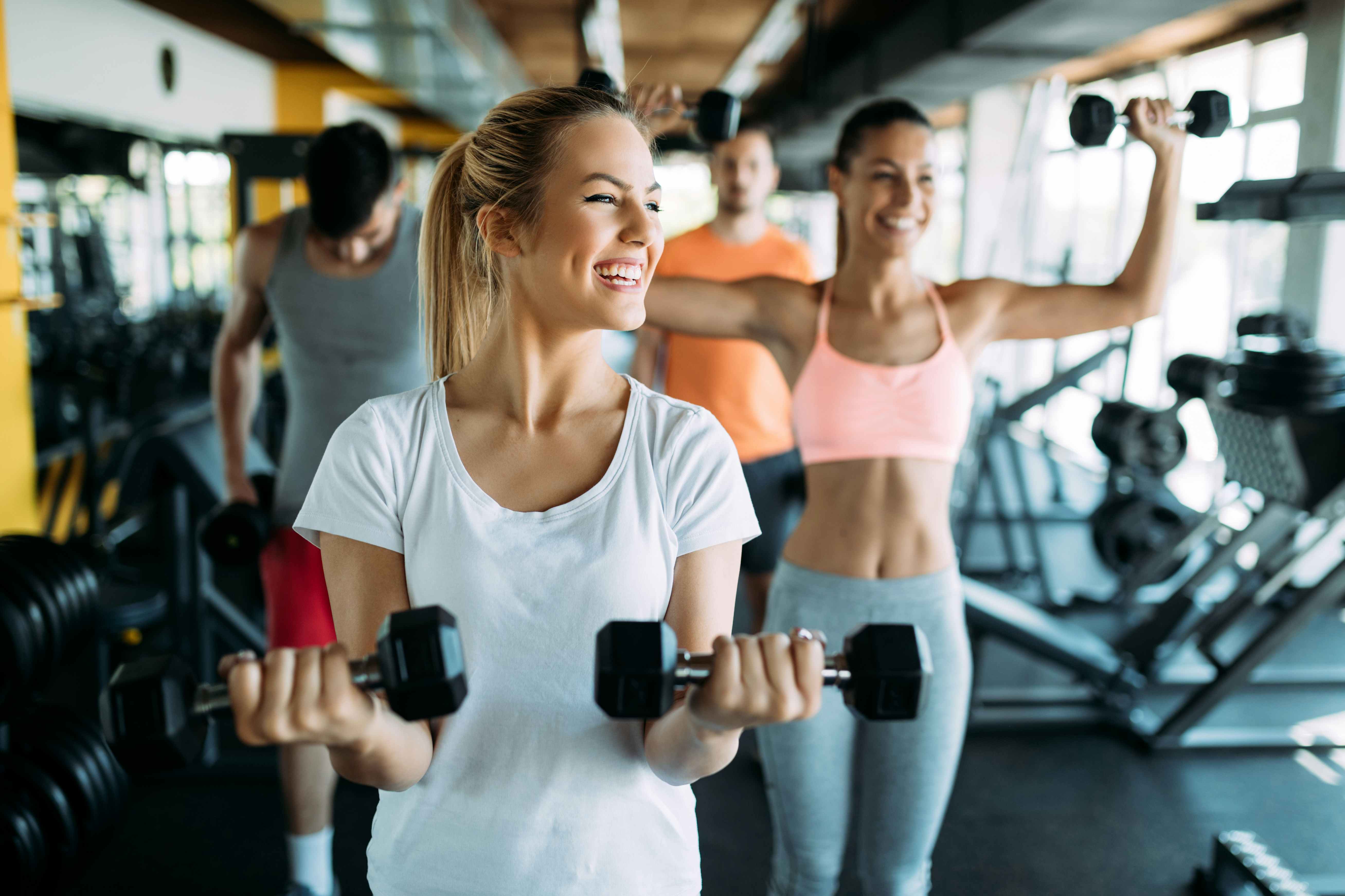 A woman lifting light weights at gym with friends