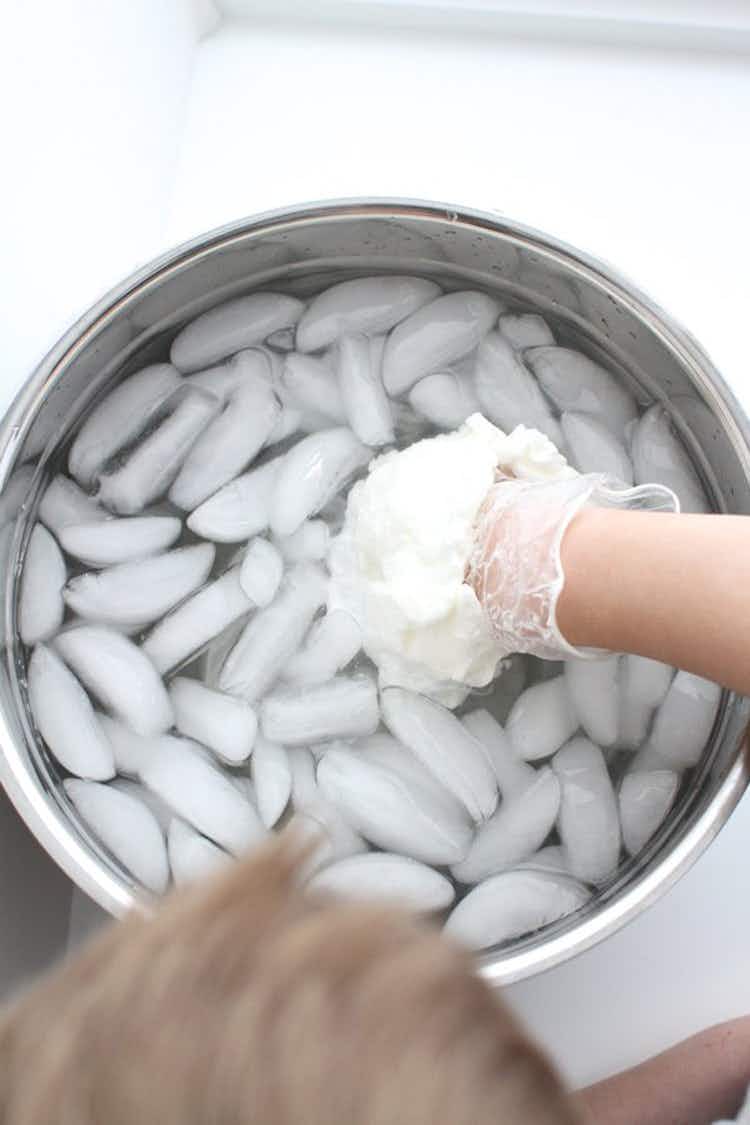 A person inserting their hand in a glove covered in shortening into a container of icy water.