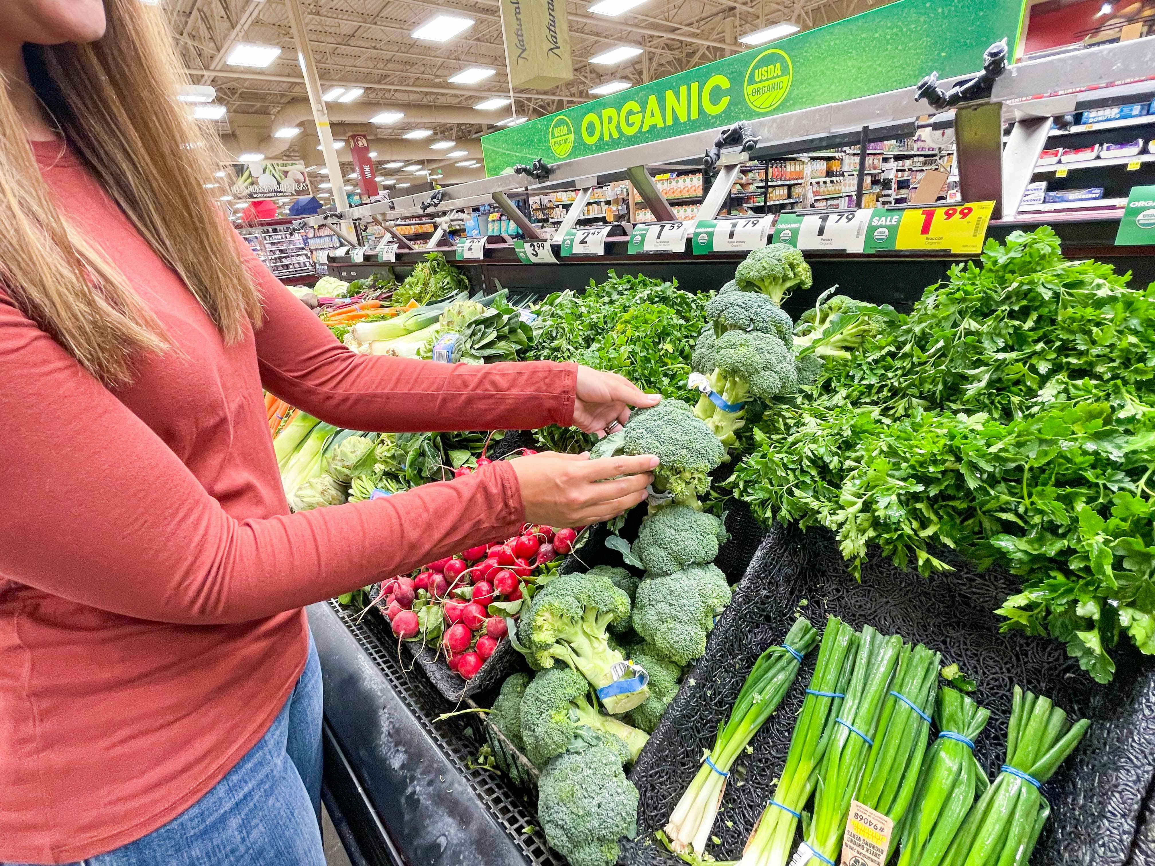 A person pulling a bundle of broccoli from a produce display in a grocery store.
