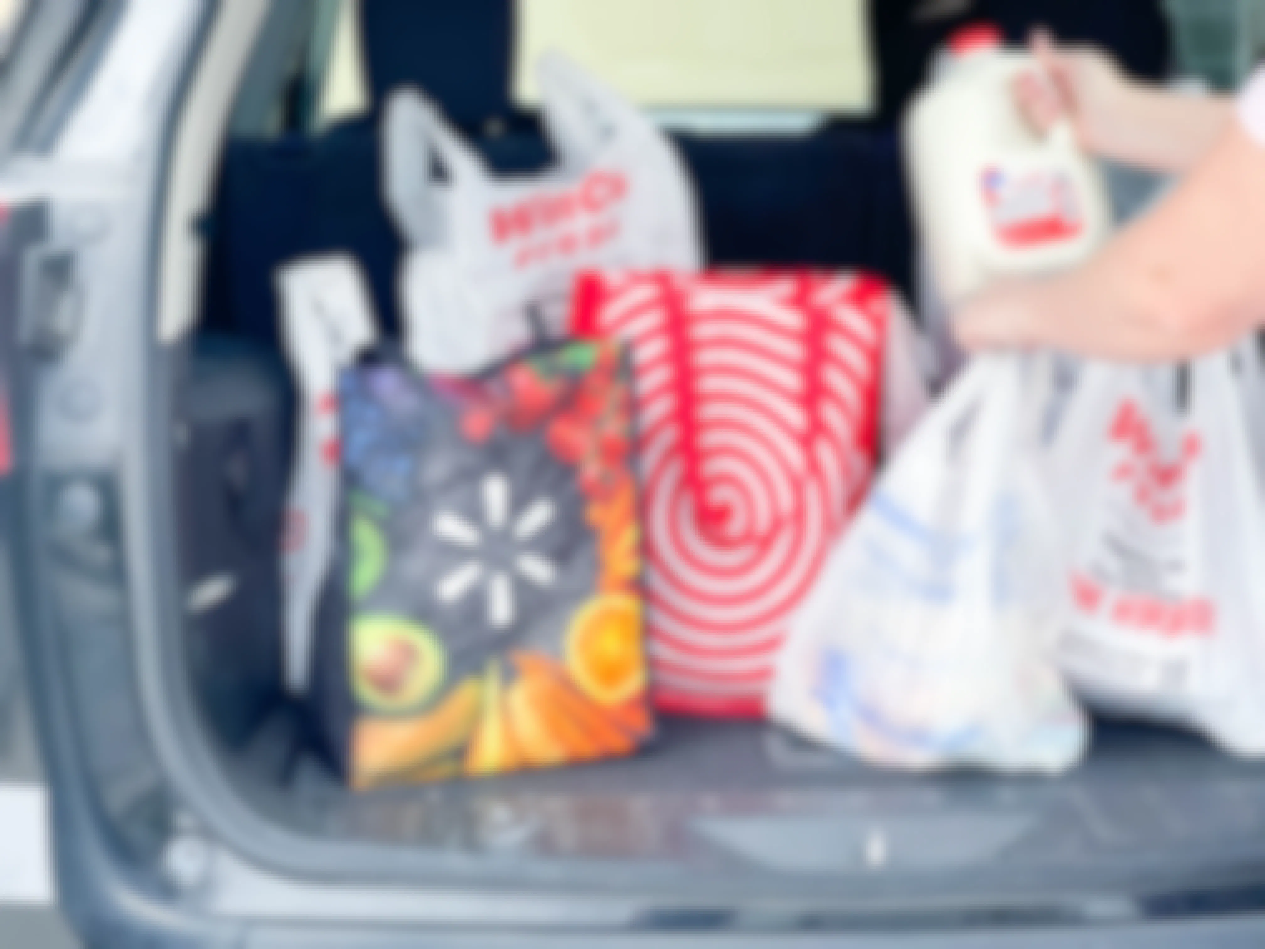A person putting a gallon of milk into the trunk of a vehicle with reusable and plastic grocery bags from Walmart, Target, and WinCo Foods.