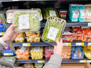 A person holding prepackaged produce in front of a shelf at a grocery store.