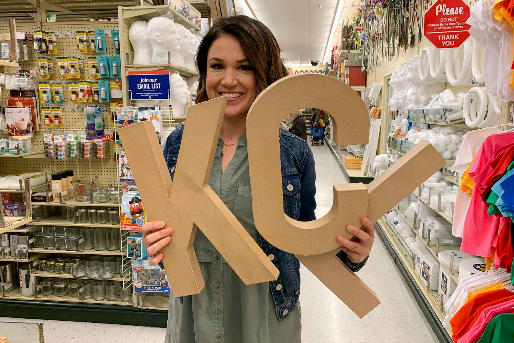 One of the owners of thekrazycouponlady.com, holding up large cardboard letters that read "KCL".