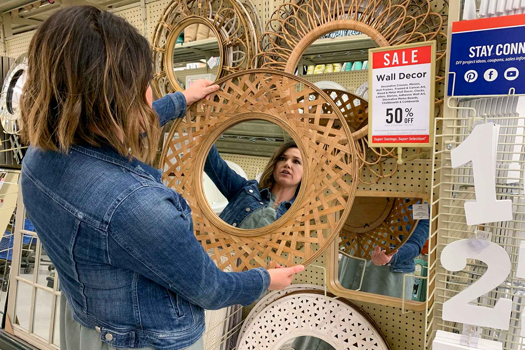 A woman looking at a mirror in an aisle filled with mirrors of varying styles and sizes.