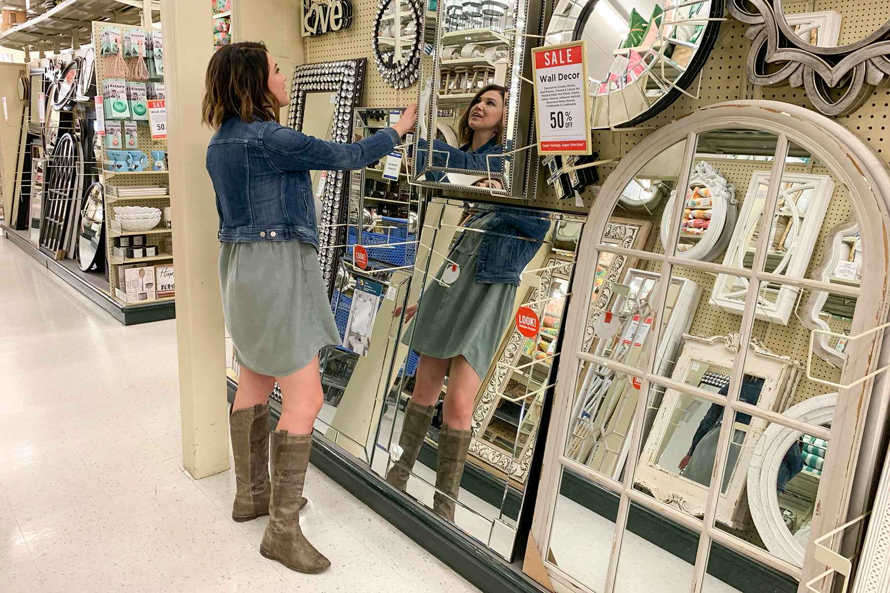 A woman looking at a mirror in an aisle filled with mirrors of varying styles and sizes.