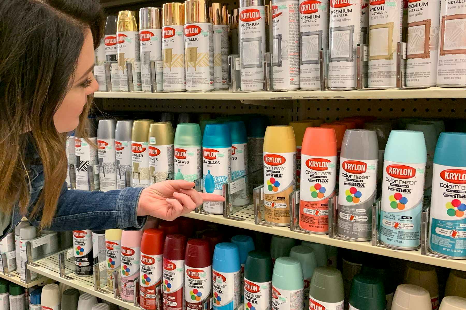 A woman pointing out an empty shelf of Krylon spray paint at Hobby Lobby.