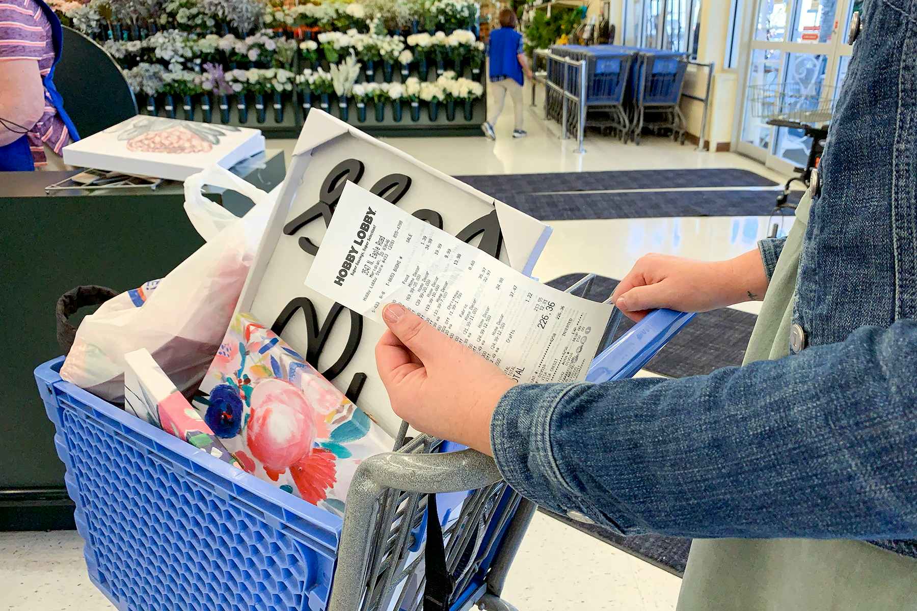 A woman holding a receipt in front of a basket filled with products at the Hobby Lobby return register.