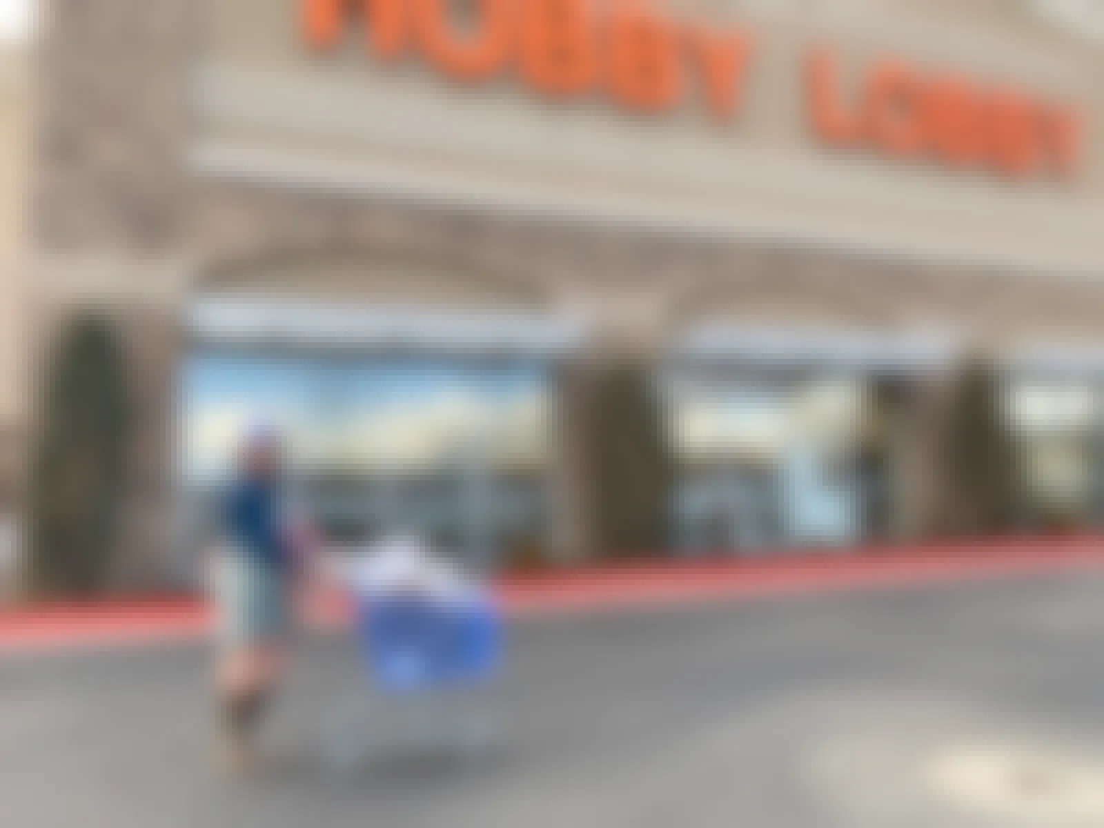 A woman pushing a cart in front of a Hobby Lobby store.
