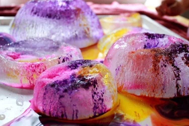 A tray with bowl-shaped ice chunks with food coloring dripping down to highlight the crackes in the ice made from salt poured on them.