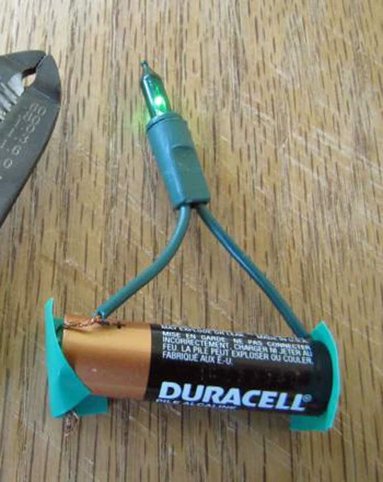A small Christmas tree light cut from a light string has a wire taped to each end of a battery.