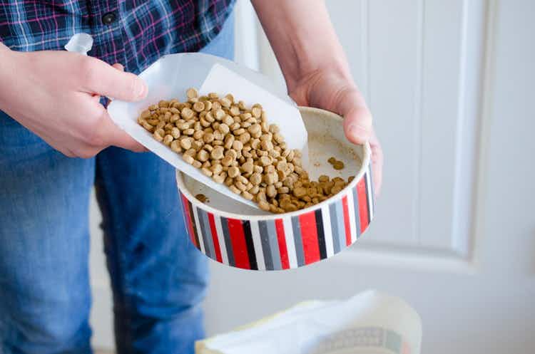 A person pouring dog food into a bowl.