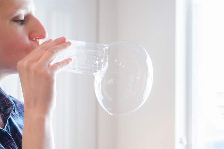 A person blowing bubbles out of a cutoff water bottle.