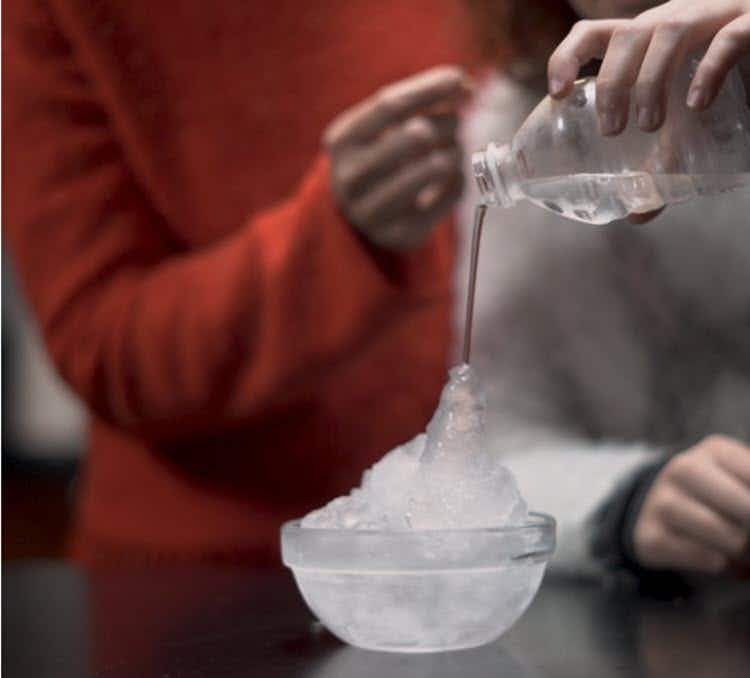 A person pouring water onto ice cubes in a bowl.
