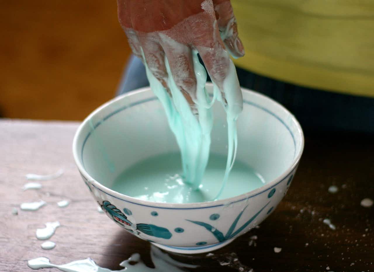 a slimy green coated hand hovers over a bowl of oobleck as a fun winter science experiments for kids