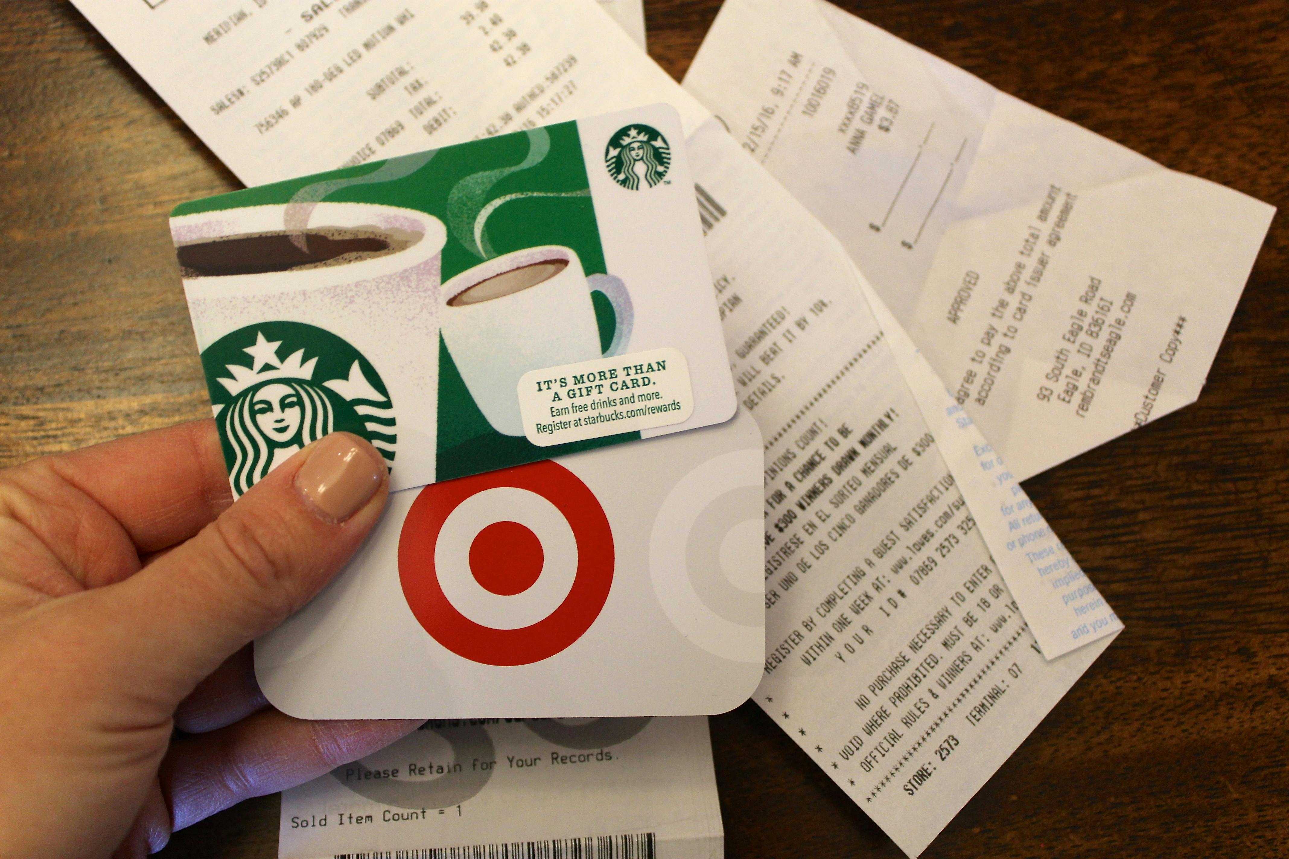 A person holding a Target and a Starbucks gift cards in their hand in front of two receipts on a table.