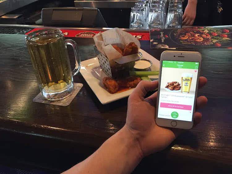 A person holding a smartphone with the Ibotta app open next to a glass of beer and plate of food.