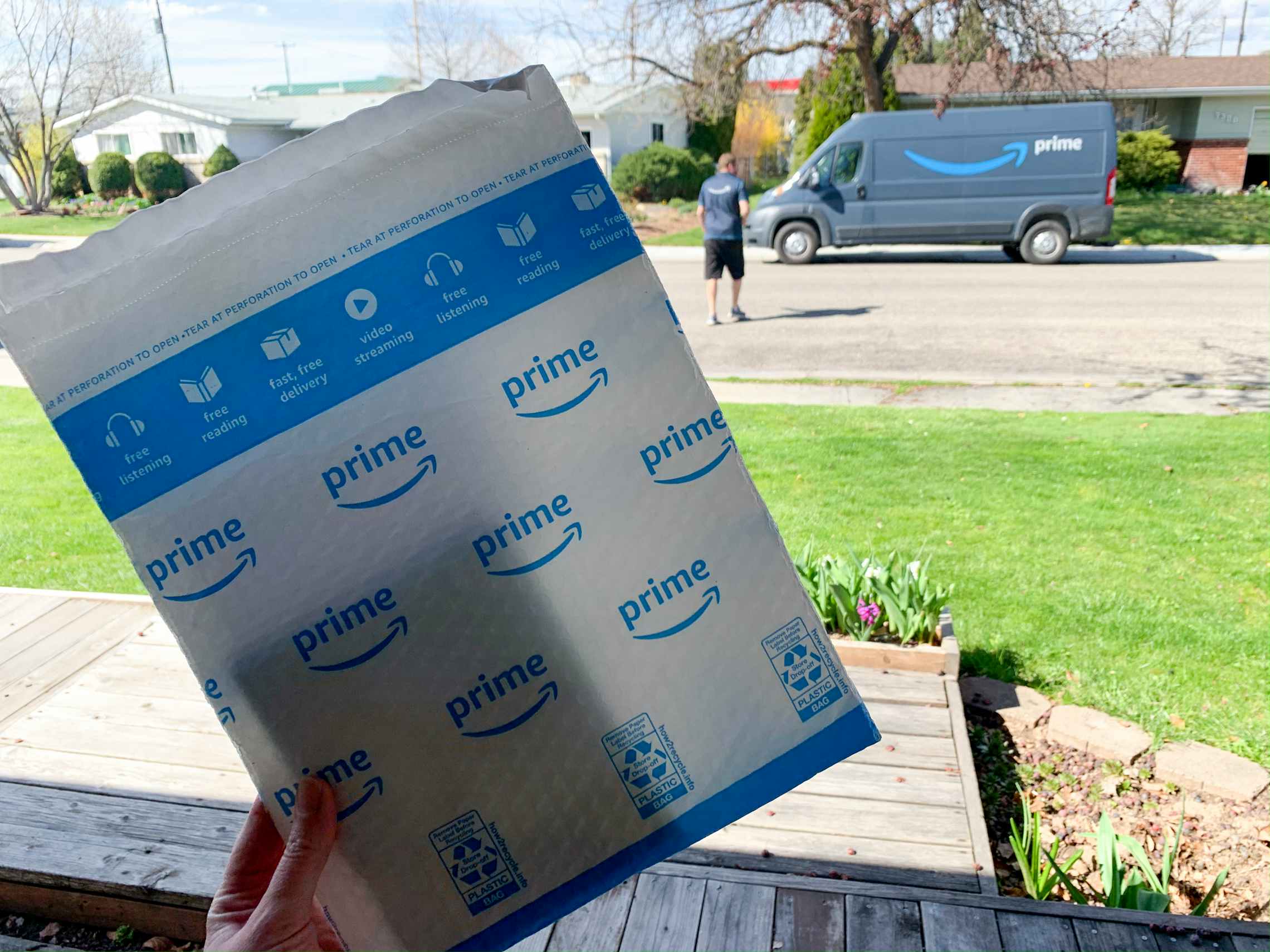 An amazon delivery package held up with a truck and delivery driver in the background.