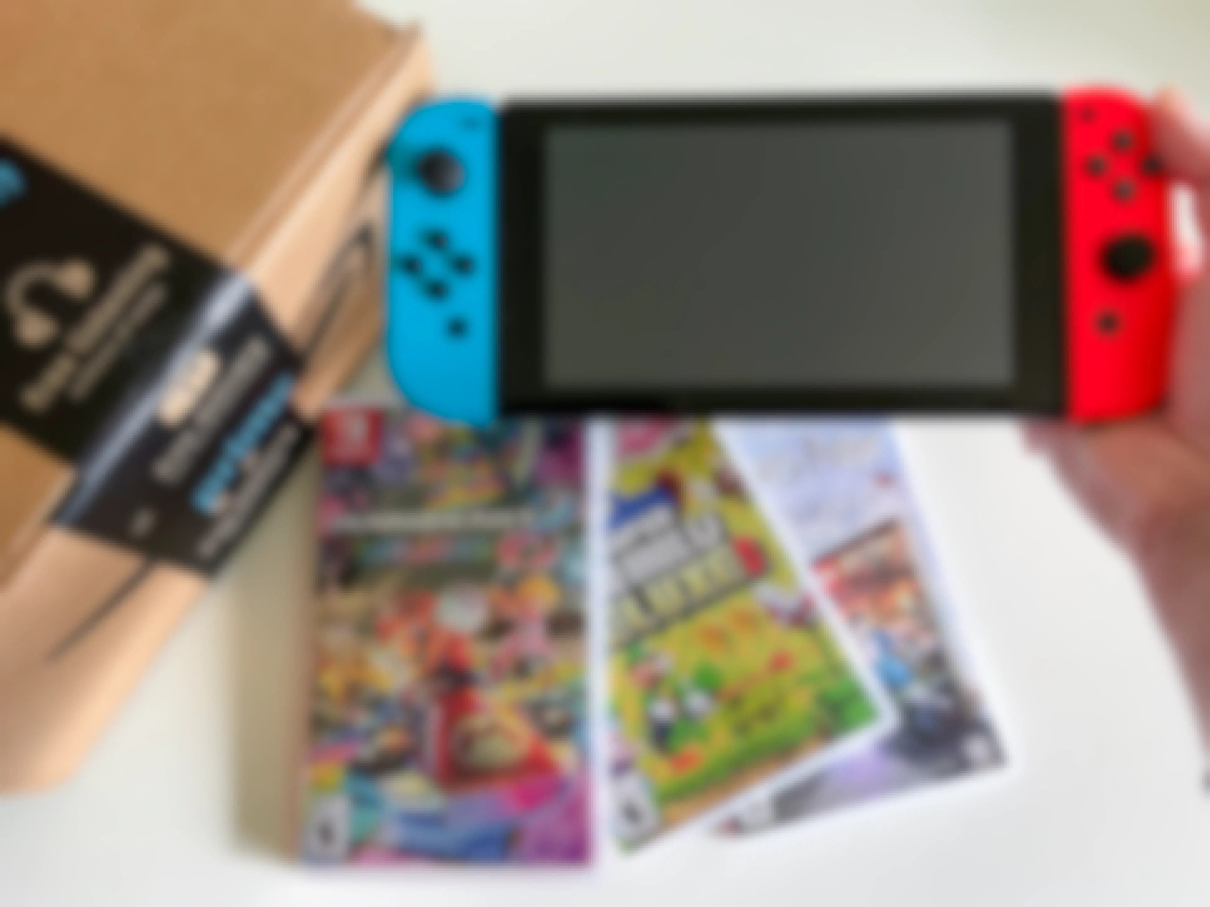 A person's hand holding up a Nintendo Switch next to an Amazon box with three Switch games below it.