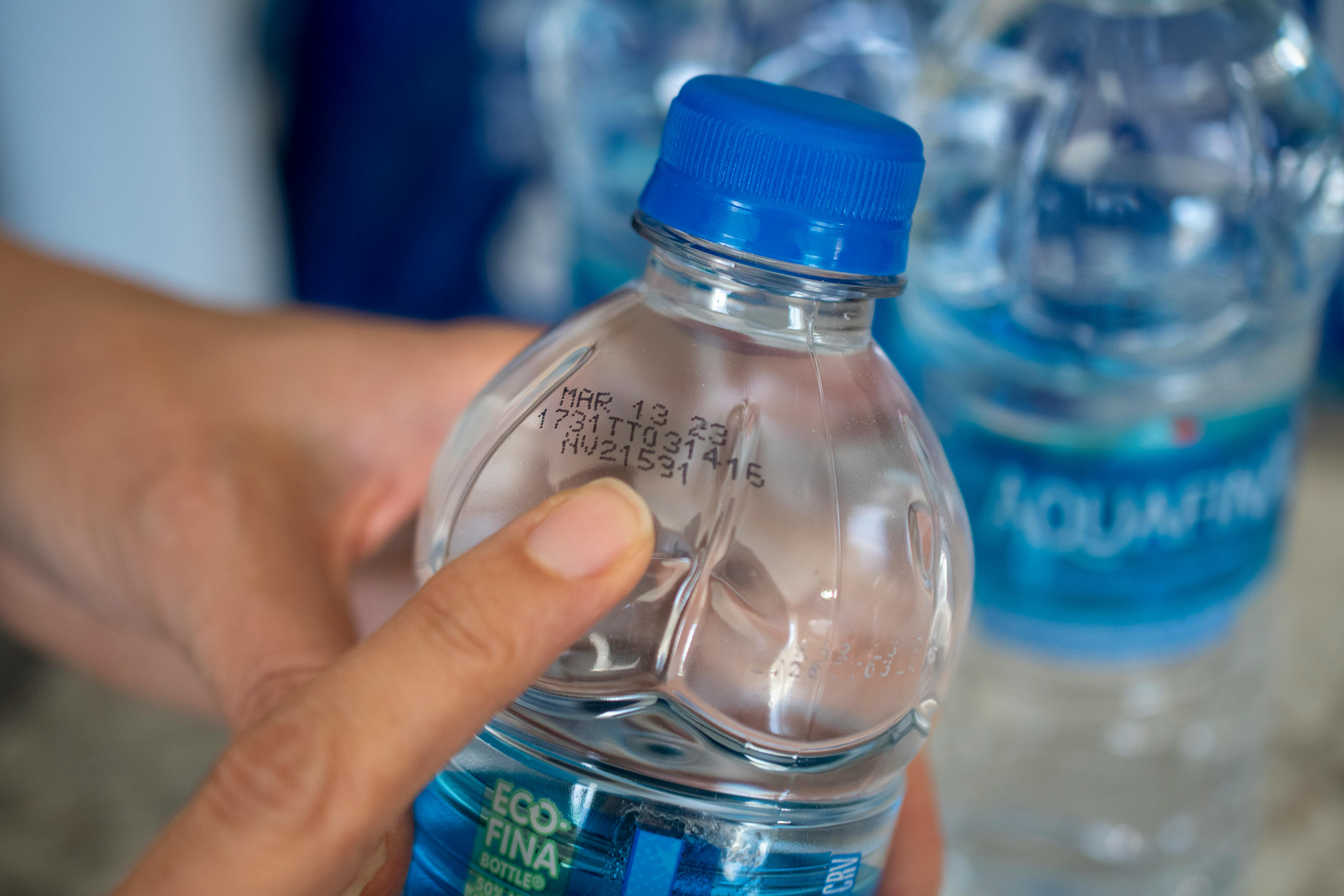 A person pointing to the expiration date on a bottle of water