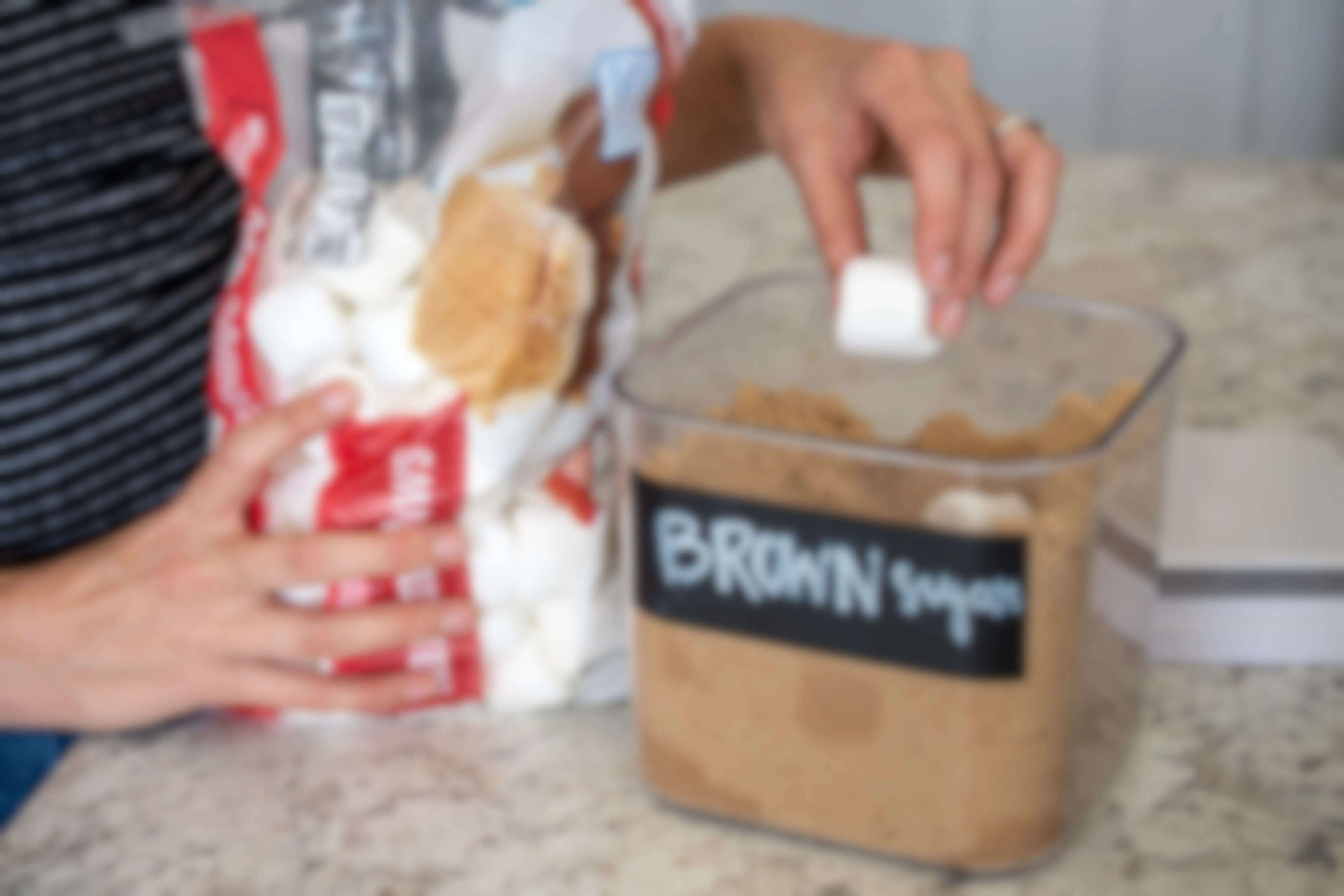 A person putting two large marshmallows inside a container filled with brown sugar.