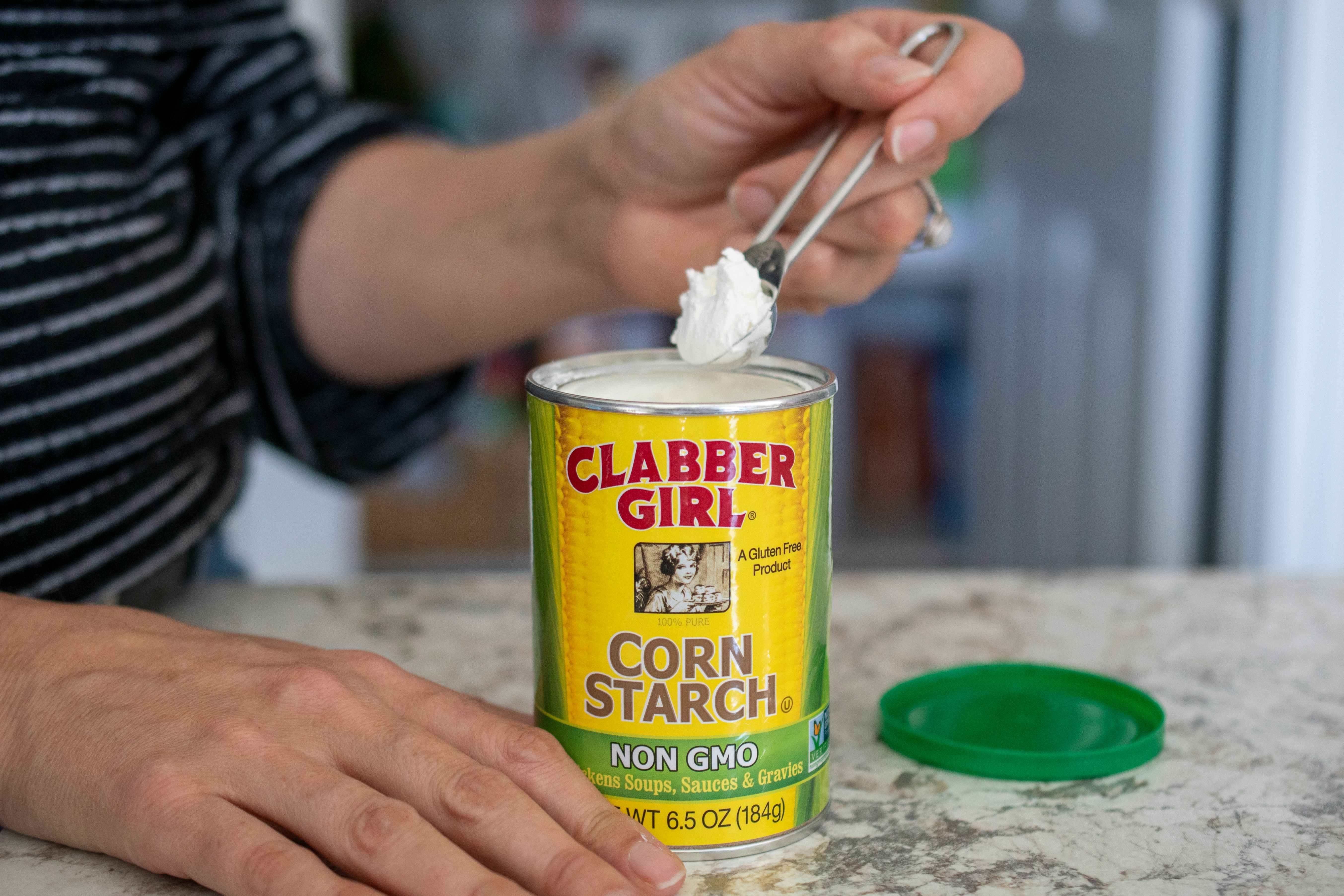 A person using a measuring spoon to scoop out corn starch from a canister