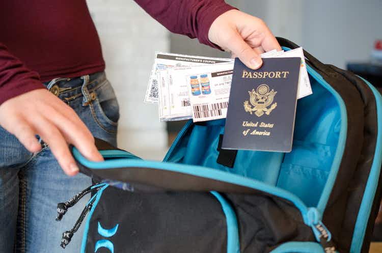 A person holding a passport and coupons by a backpack.