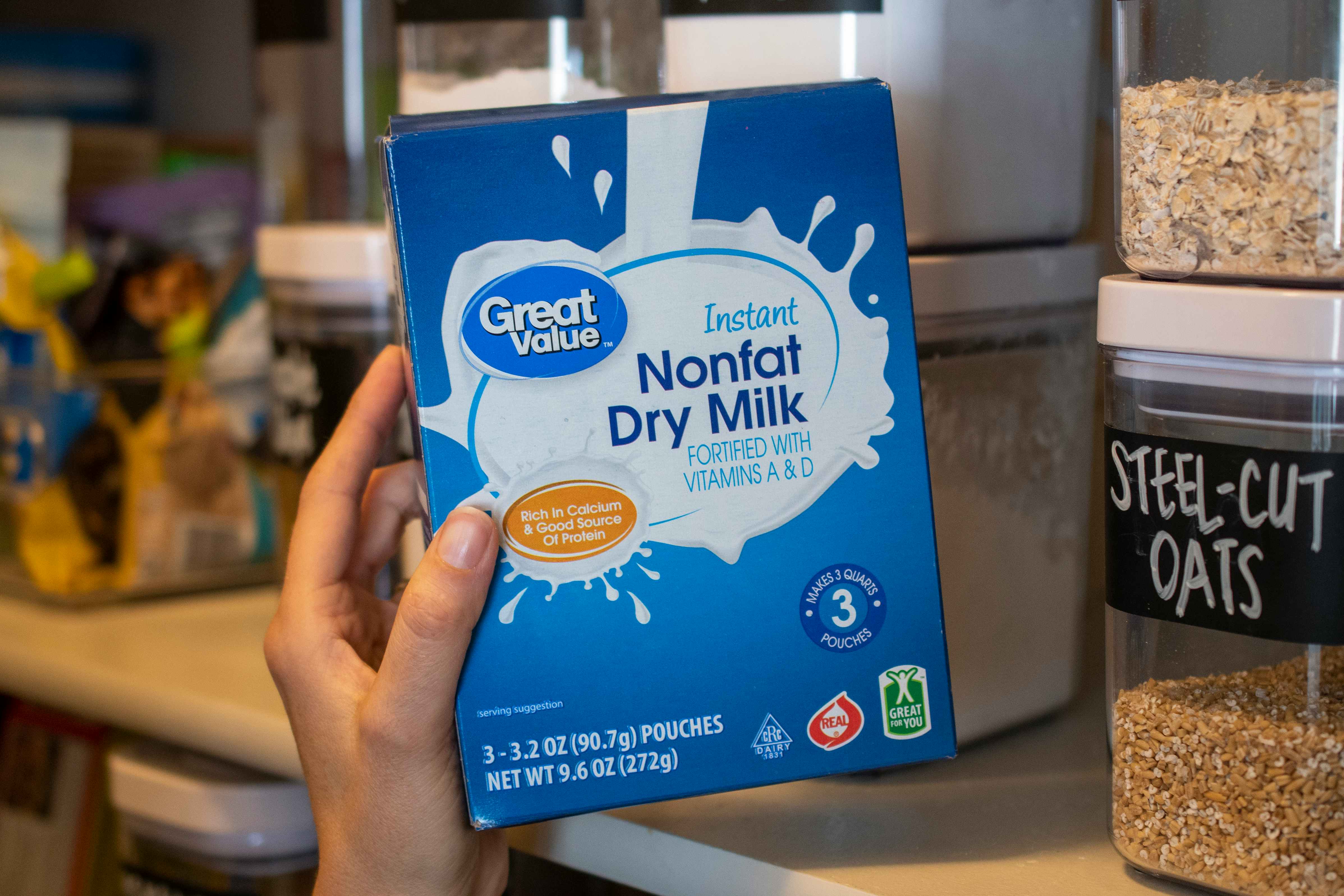 A person holding a box of Instant nonfat dry milk next to a shelf in a pantry