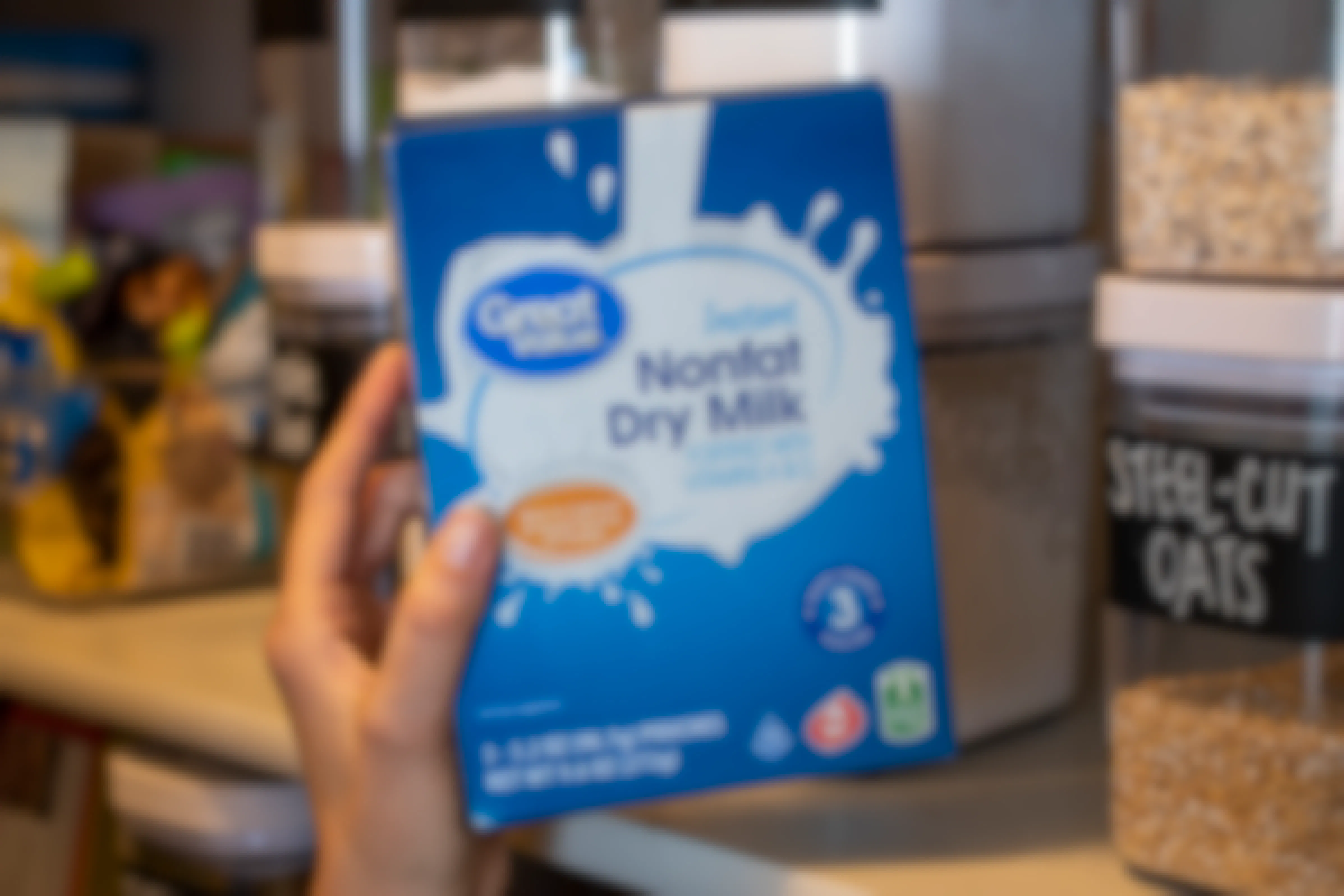 A person holding a box of Instant nonfat dry milk next to a shelf in a pantry