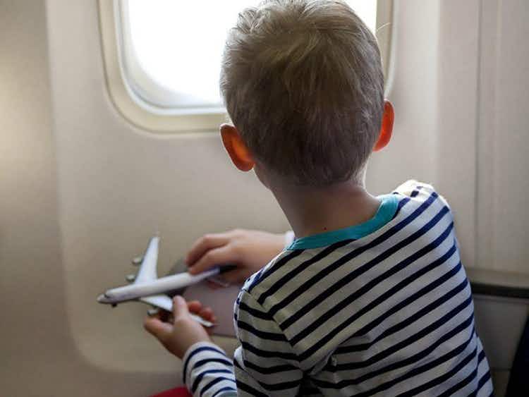 boy holding toy airplane looking out window of plane