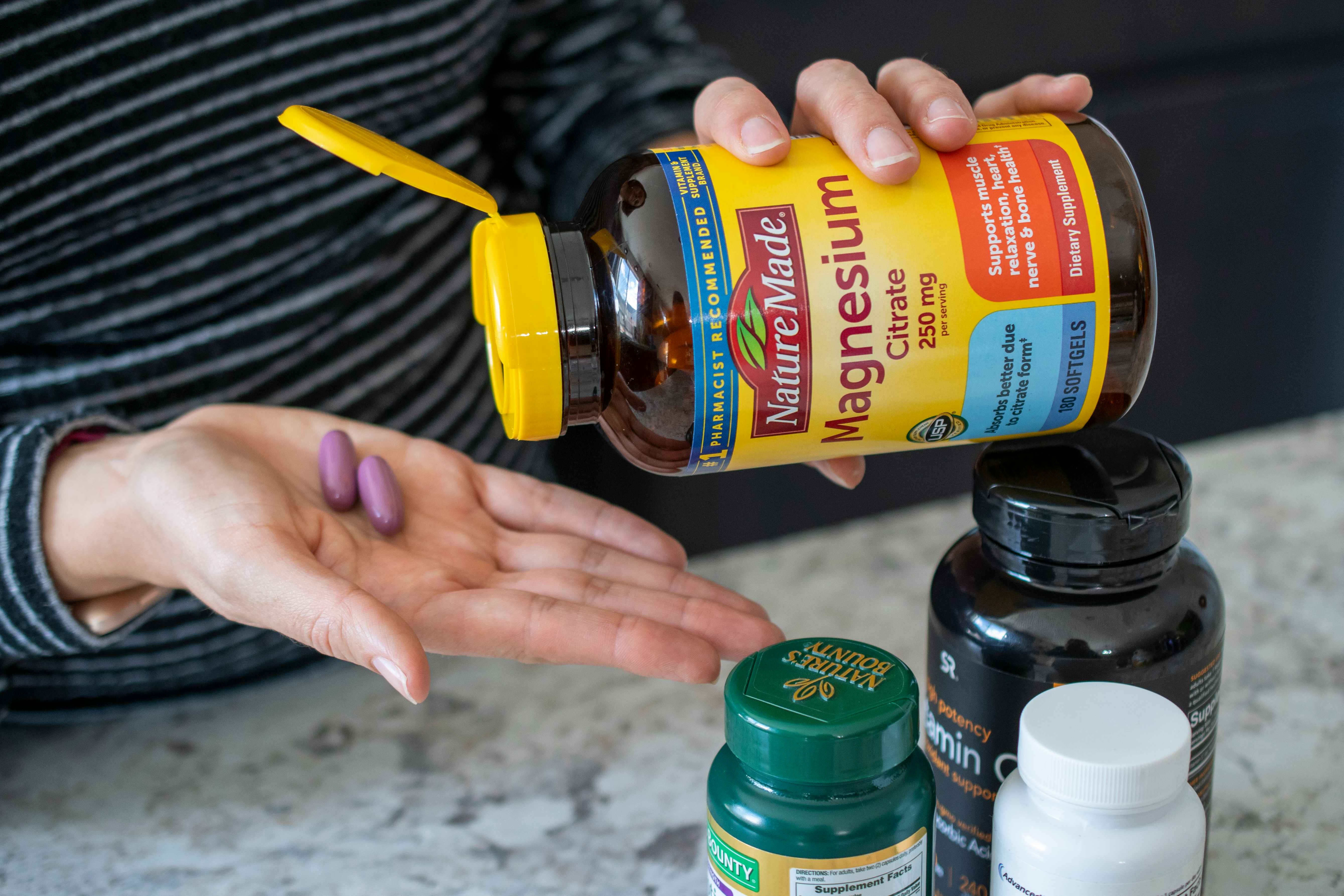 A person pouring two vitamins from a bottle into the palm of their hand