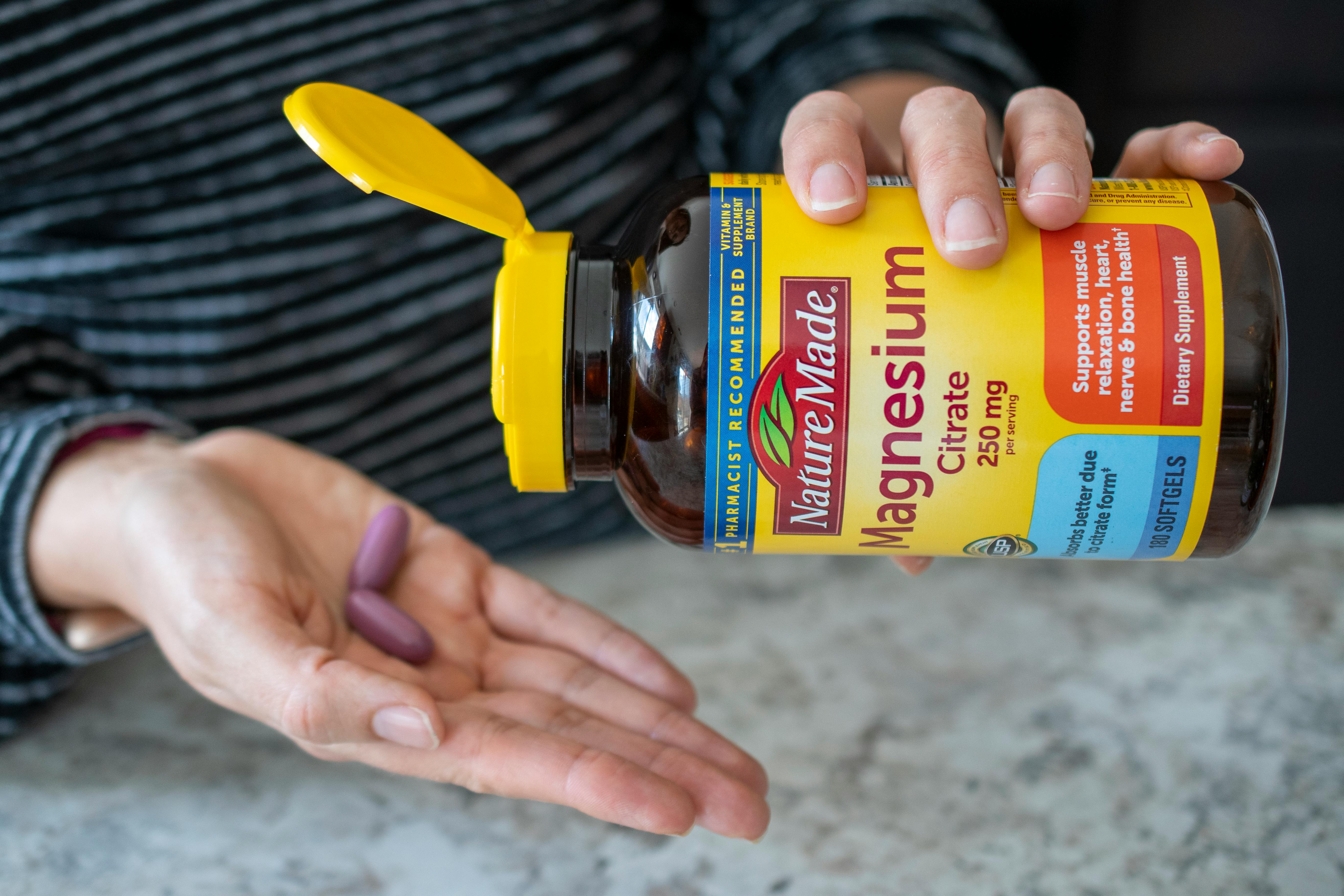 A person pouring two vitamins from a bottle into the palm of their hand
