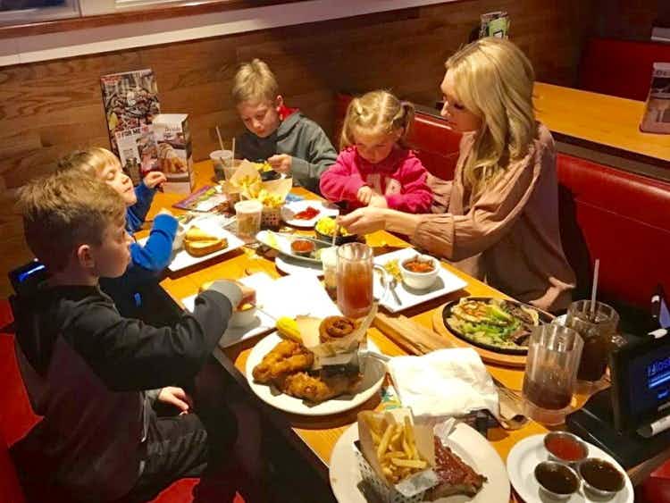A family sitting in a booth at Chili's, the table covered in different plates of food, drinks, and napkins.