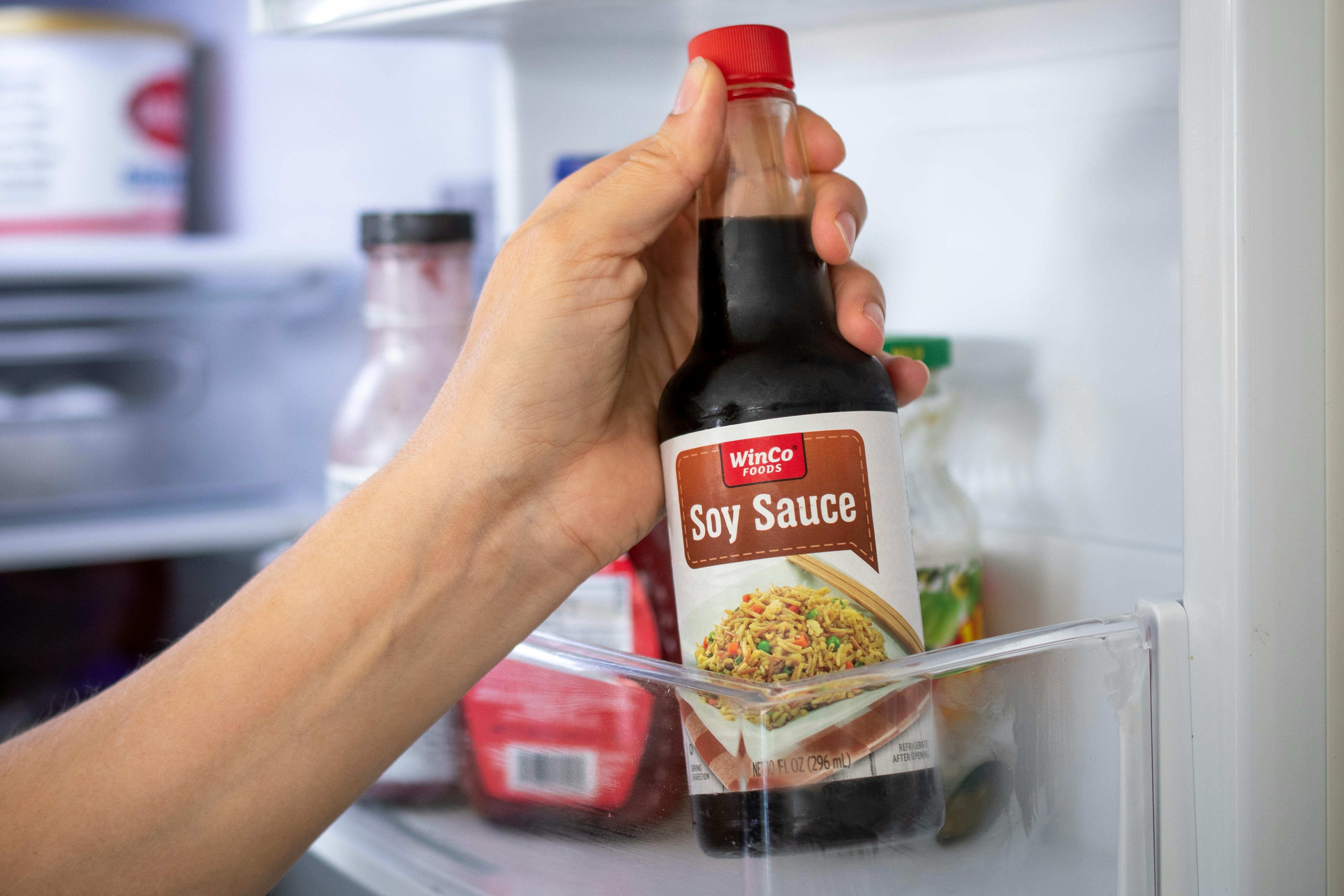 A person pulling a bottle of soy sauce from the fridge
